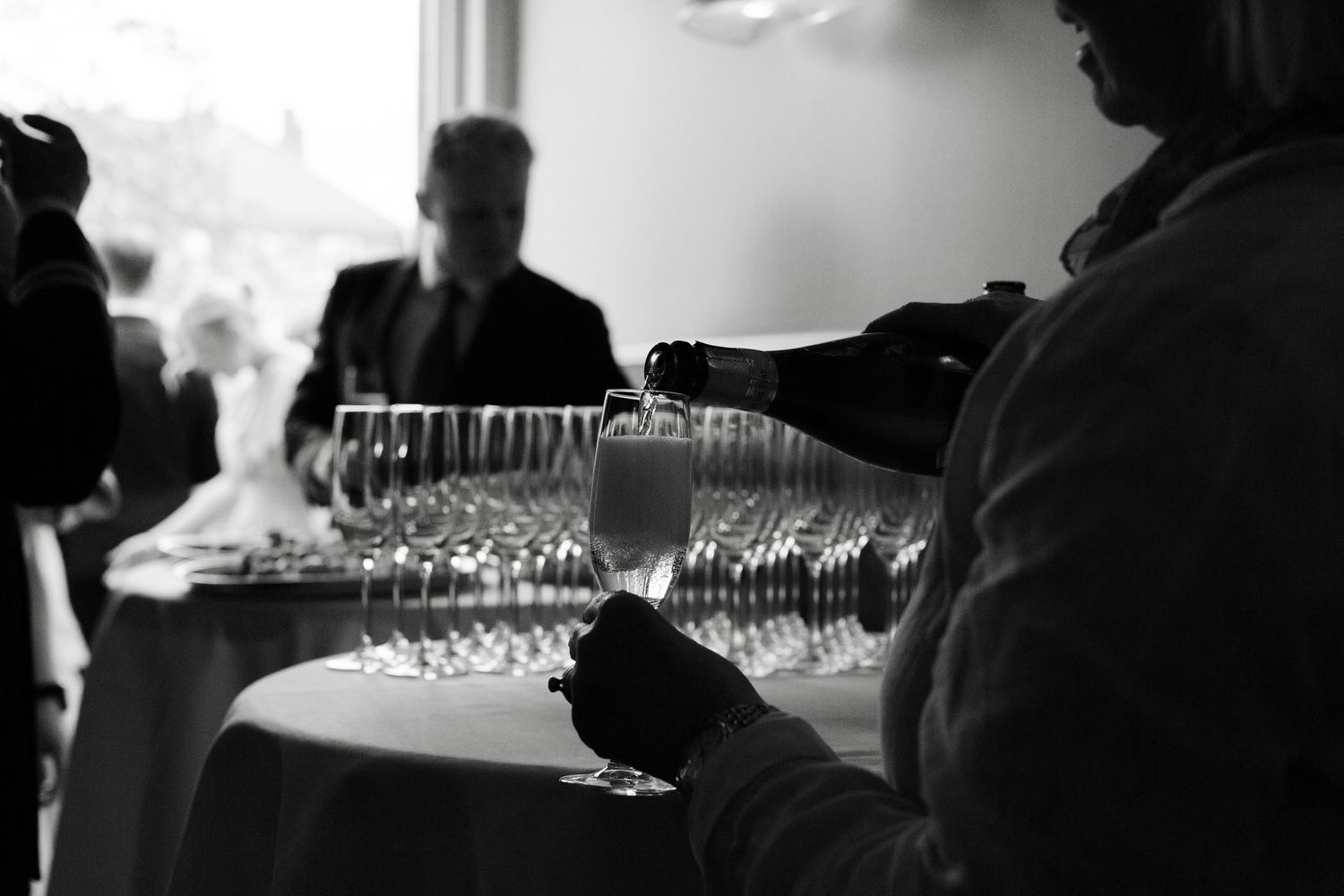Elegant black and white photo of champagne being poured into glasses at a wedding reception.
