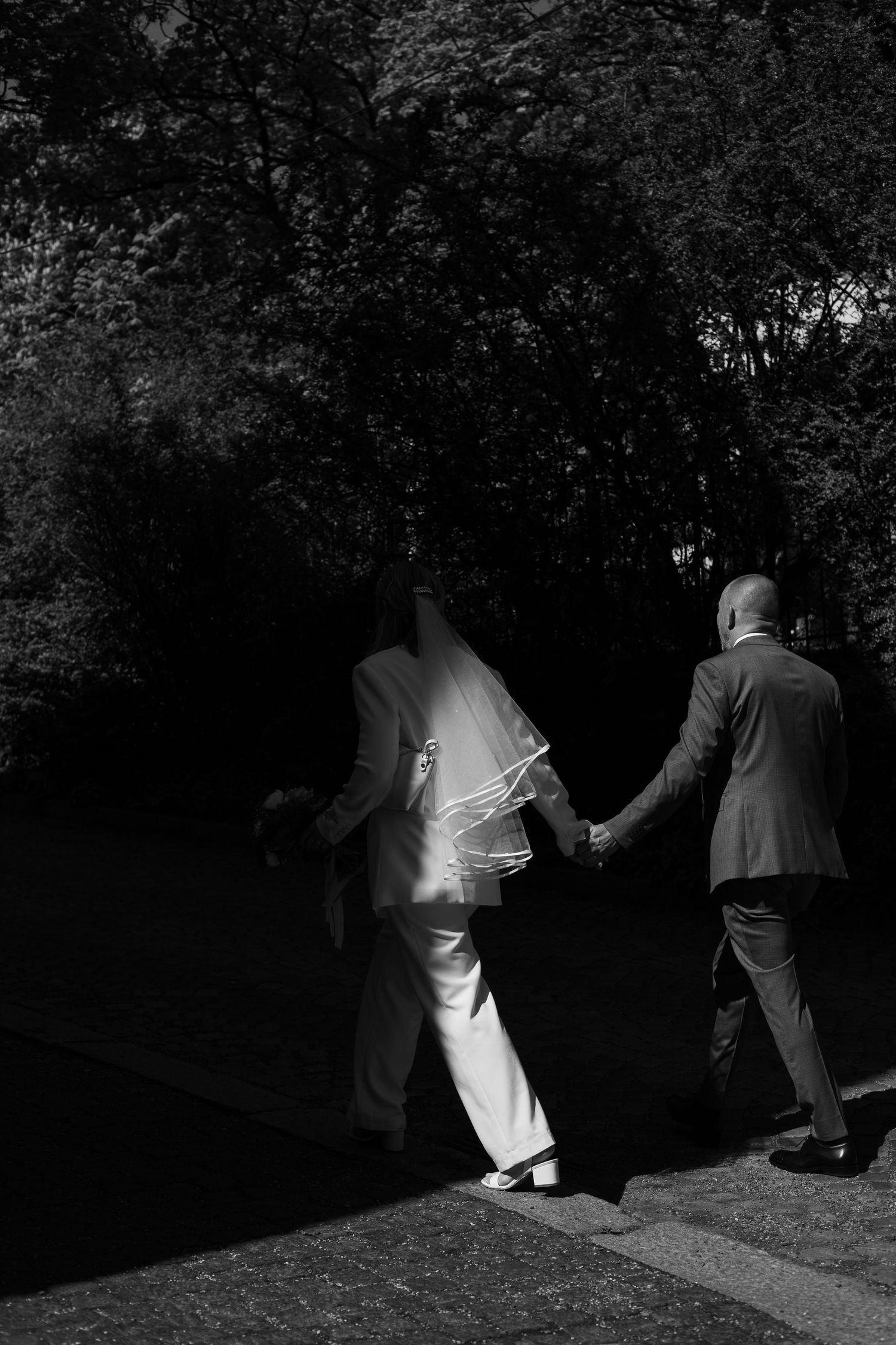 Dramatic black and white wedding photos showing silhouettes walking through a dark garden setting.