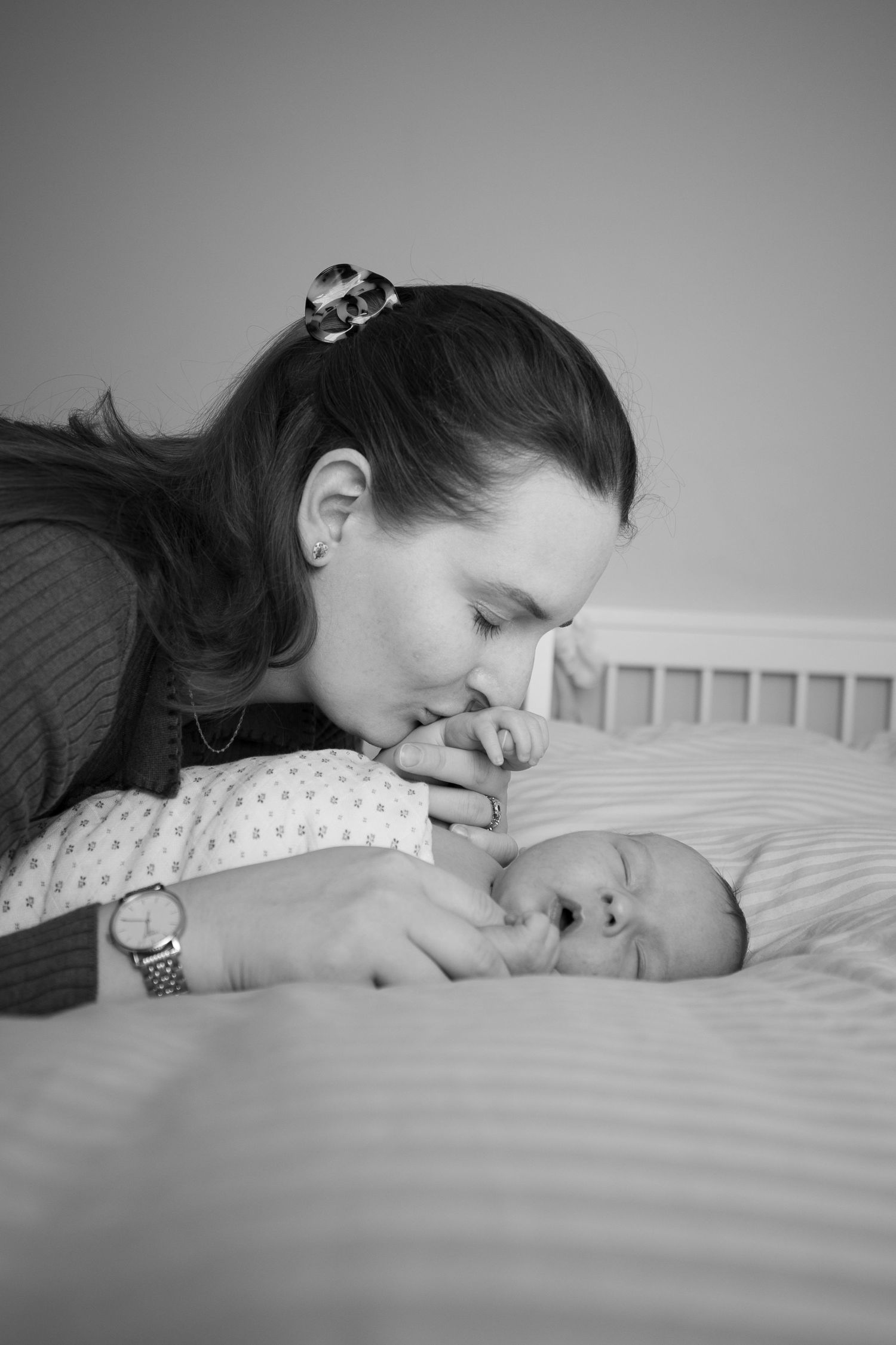 Black and white portrait of tender moment between parent and newborn on bed.