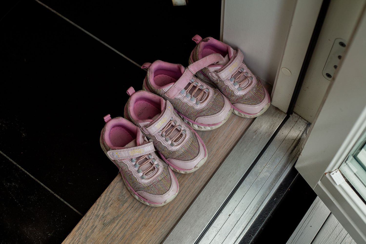 Pink baby shoes lined up neatly by a white window sill.