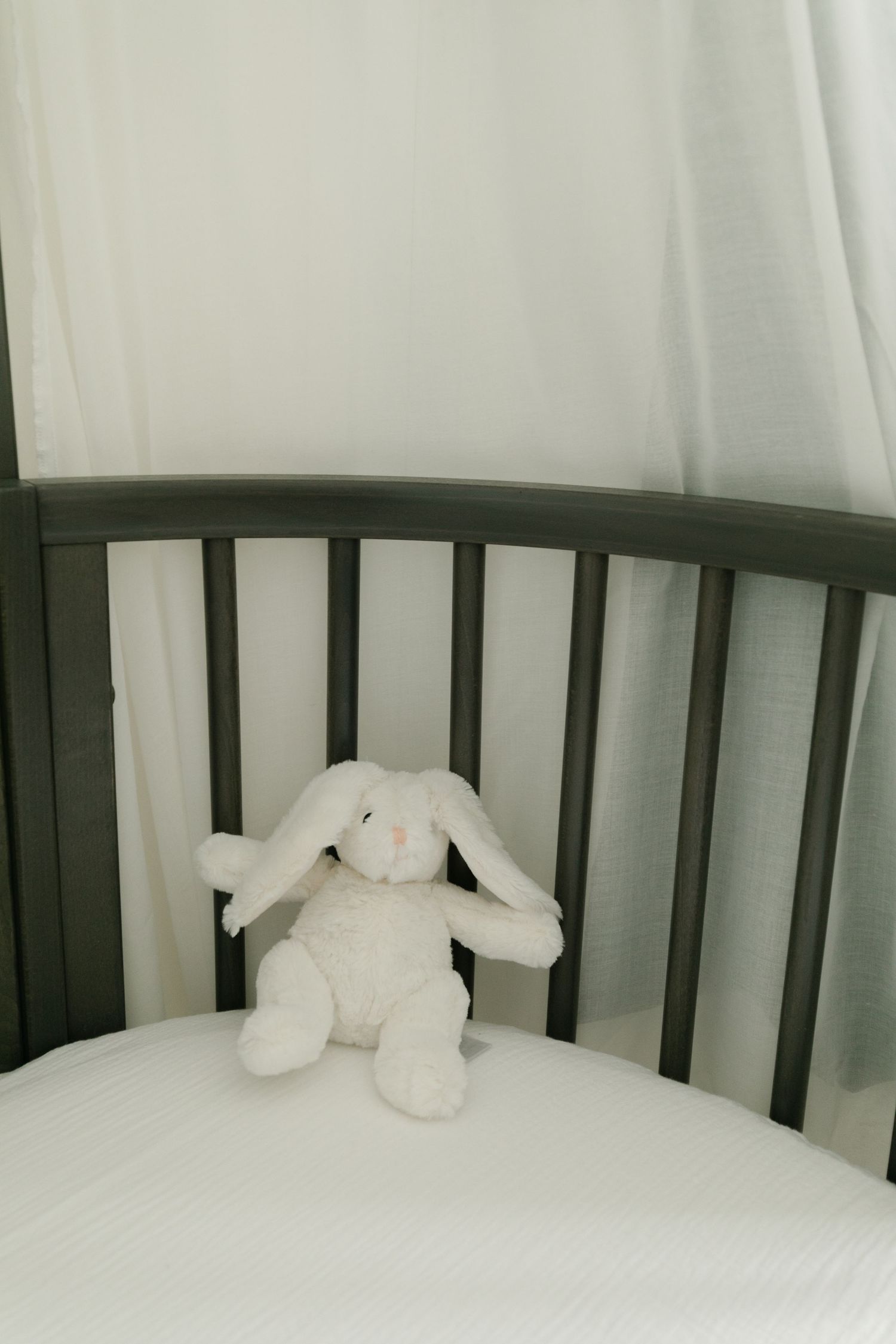 White plush bunny toy sitting alone in a gray crib.