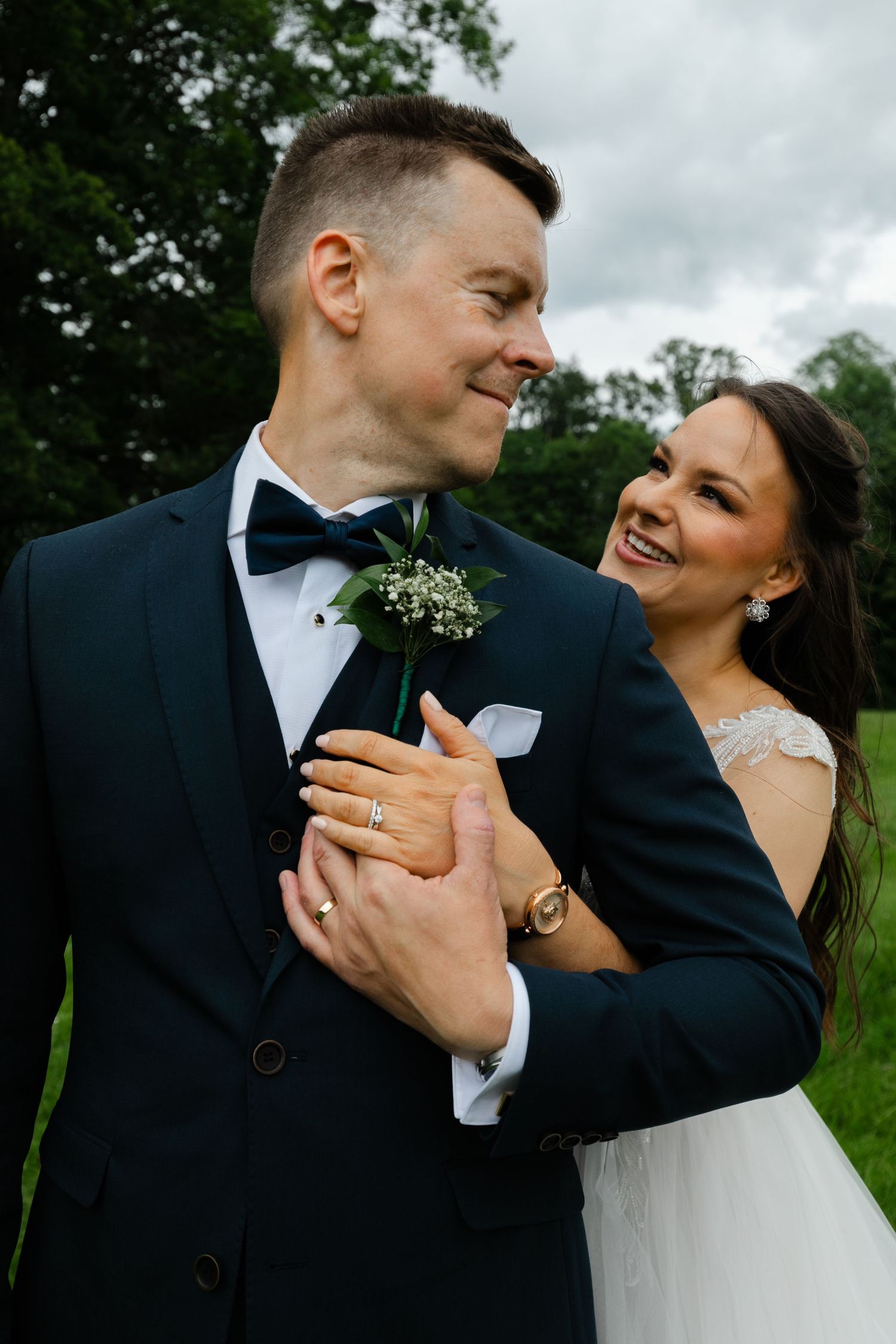 Candid wedding portrait showing couple laughing together on grassy hill.