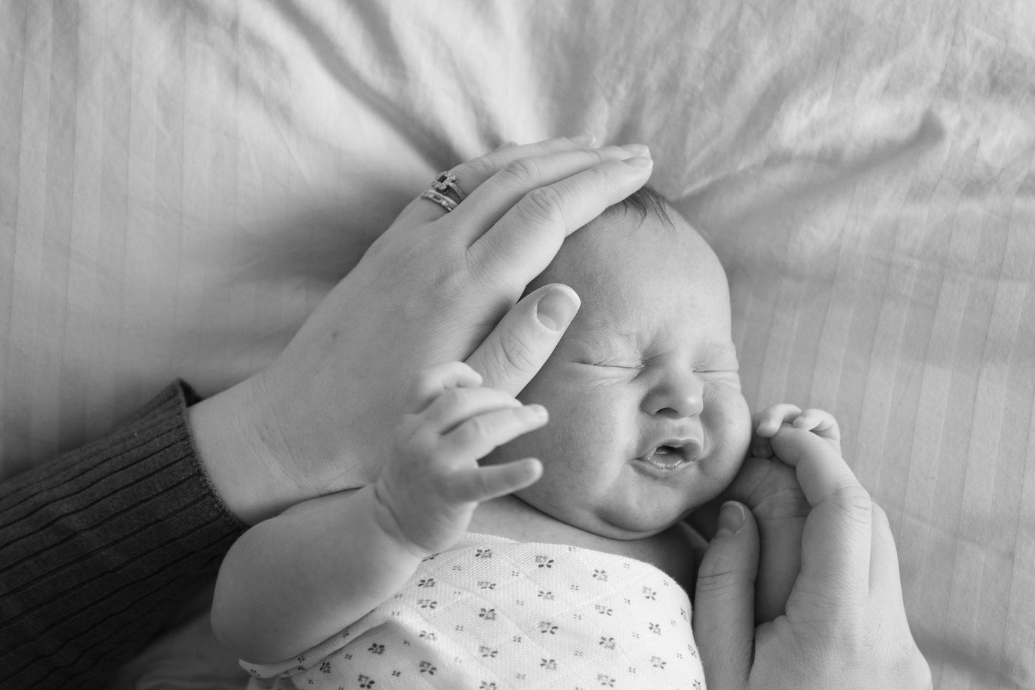 Black and white image of a hand gently touching a crying baby's head.
