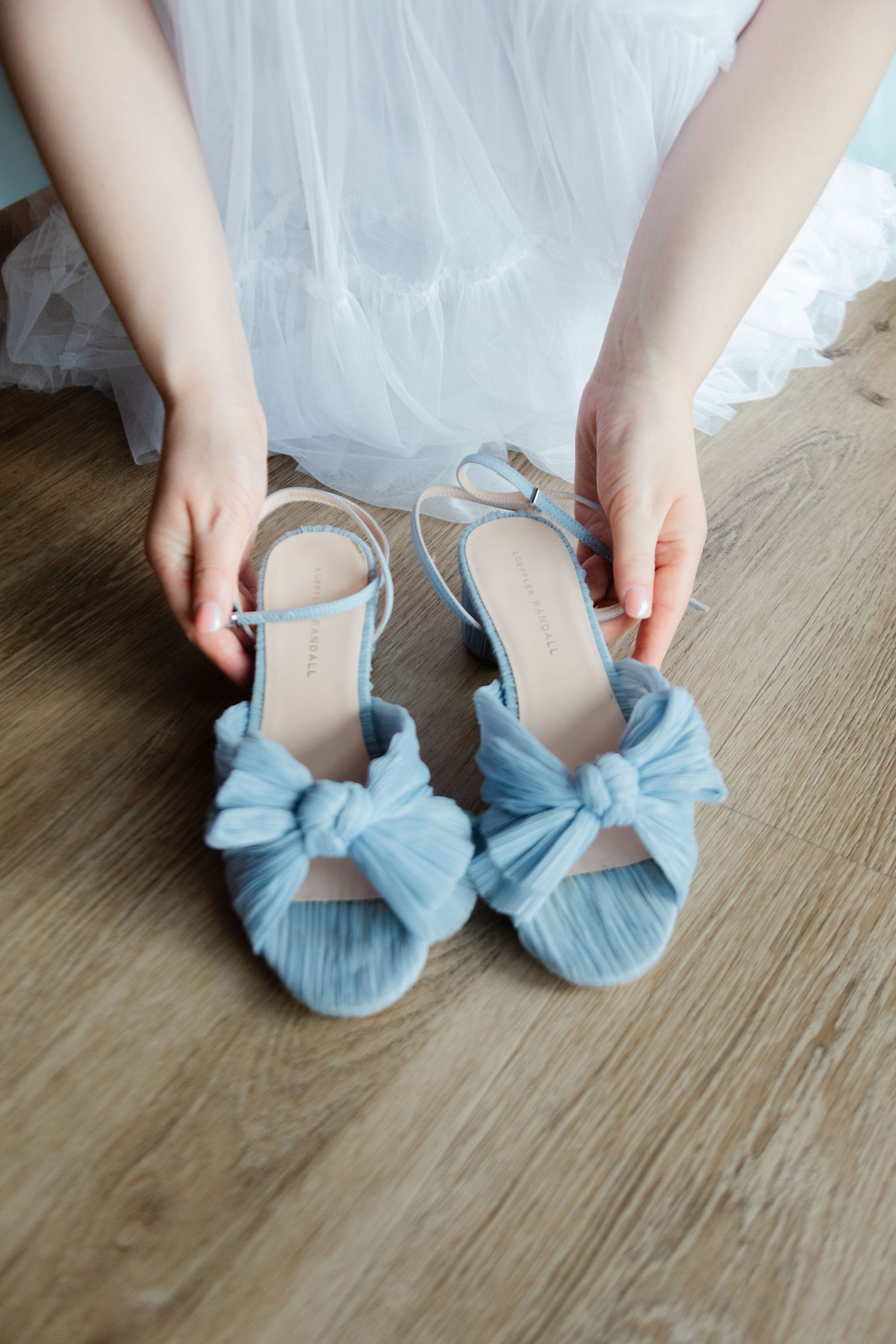 Light blue bow wedding shoes being put on against a wooden floor.