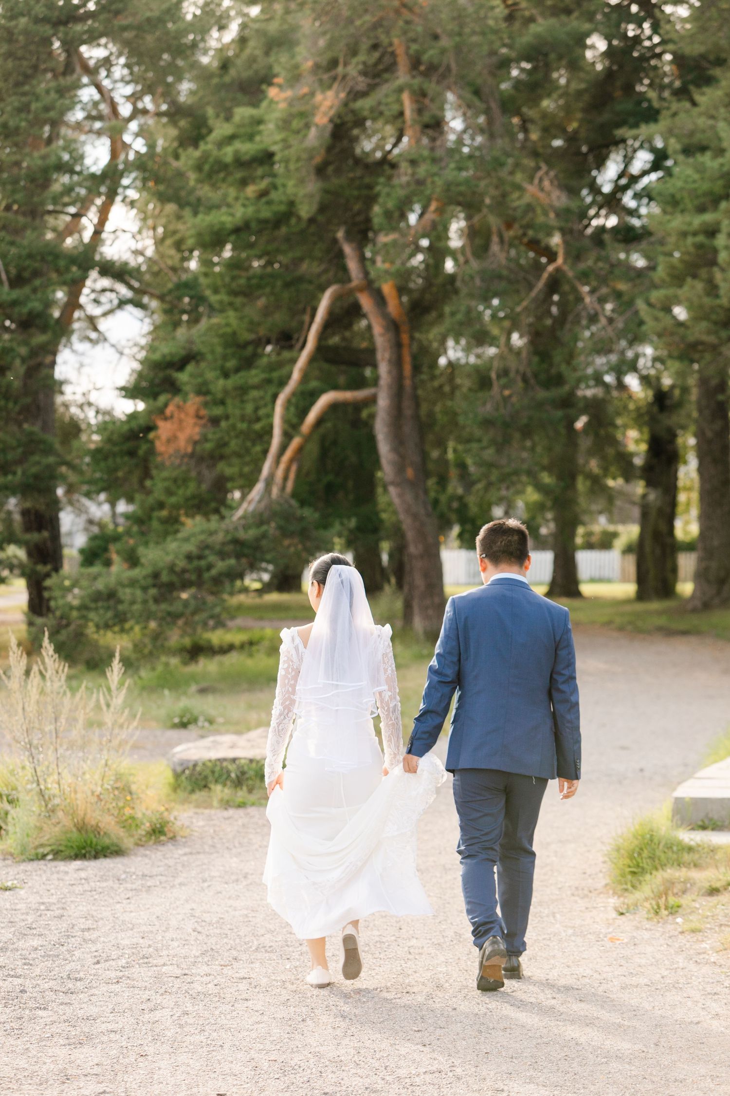 Couple in wedding attire walking along a tree-lined path.
