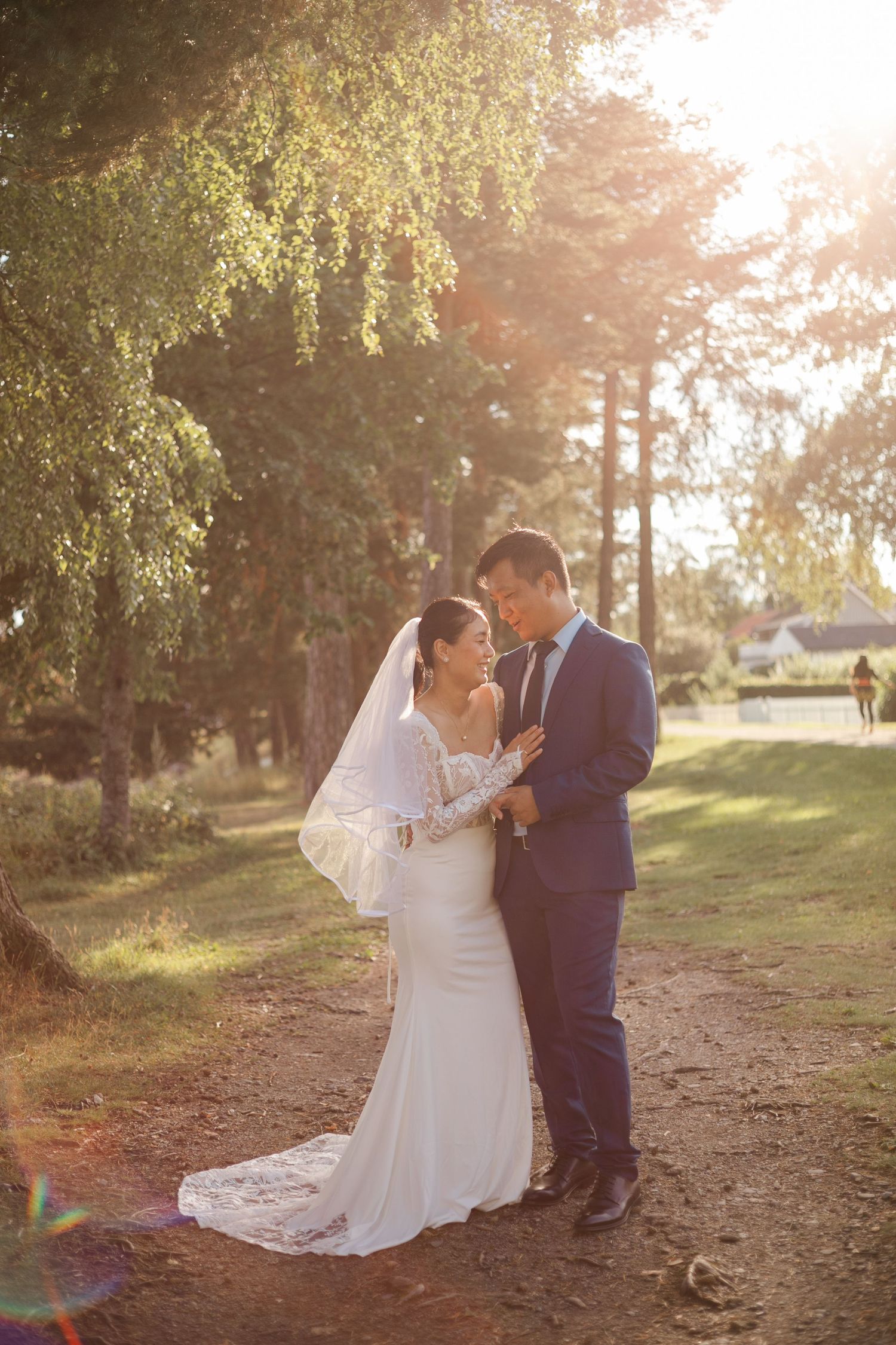 A couple shares a romantic moment on a sunlit wooded path during their outdoor wedding photo session.