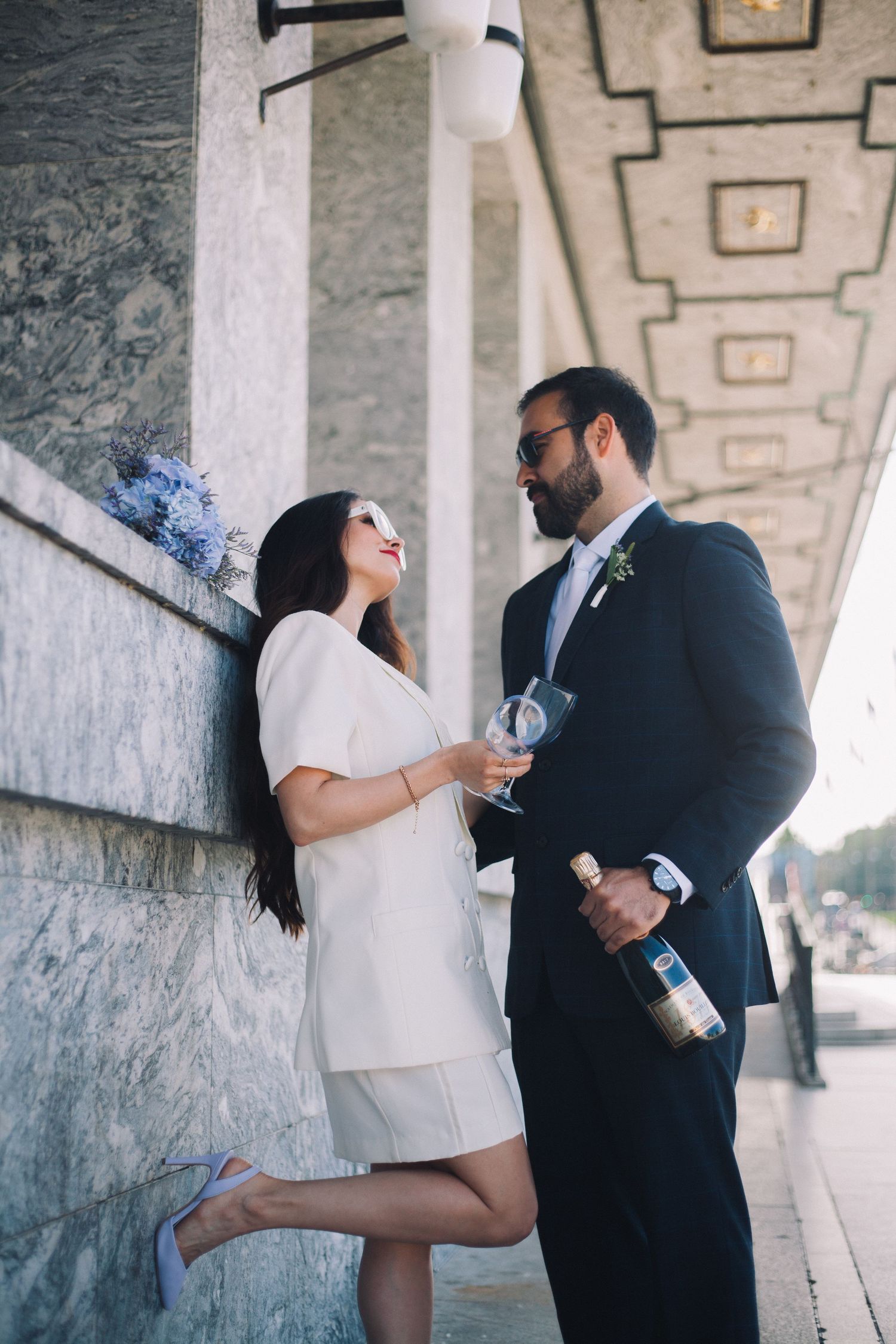 Playful couple sharing drinks and laughing under an architectural colonnade.