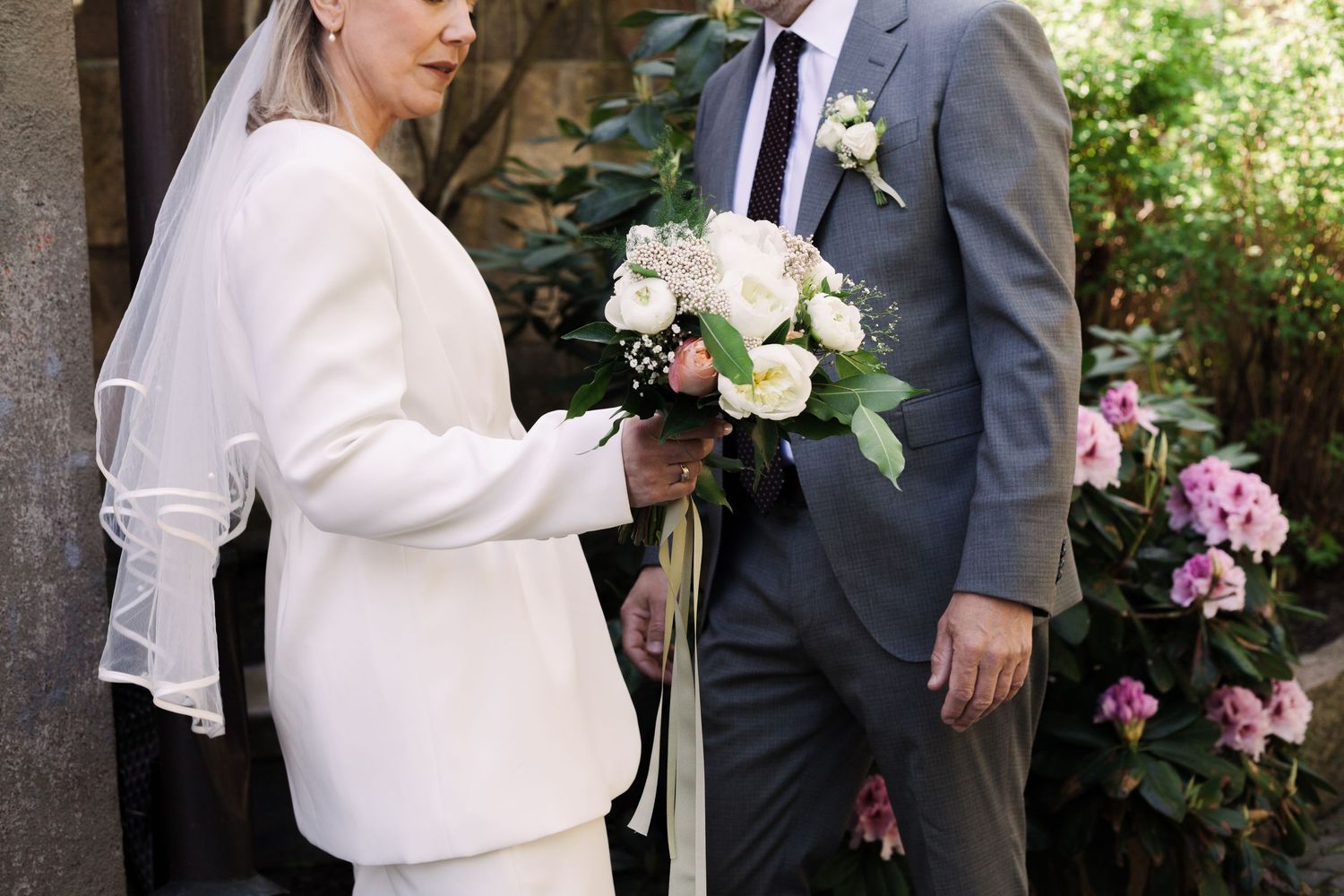 A couple sharing an intimate moment against a stone wall with flowering plants.