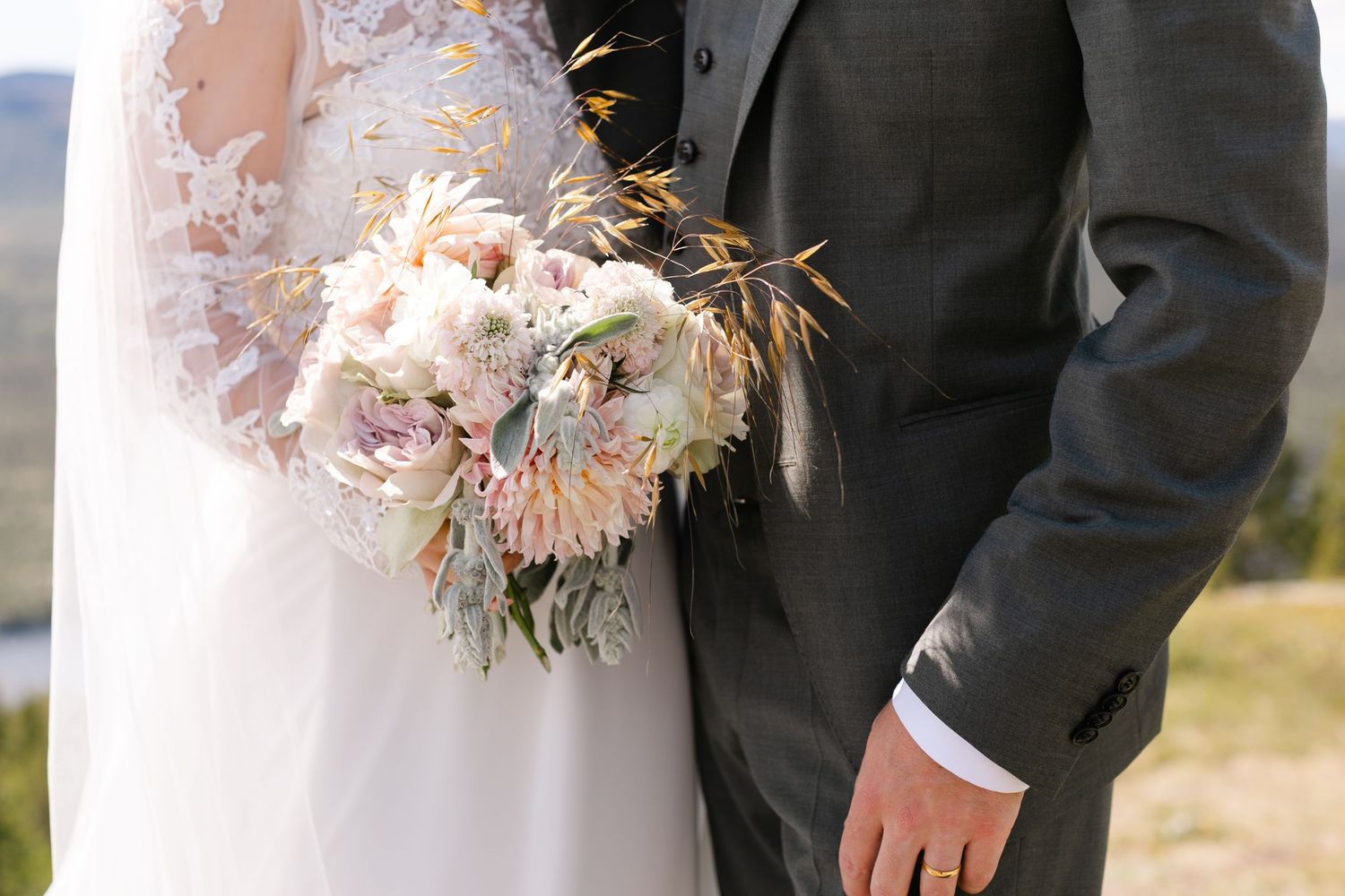 Bride and groom standing together, bride holding a blush pink and white floral wedding bouquet with greenery.