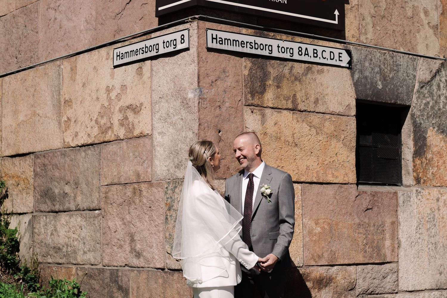 Wedding couple posing against stone wall architecture.