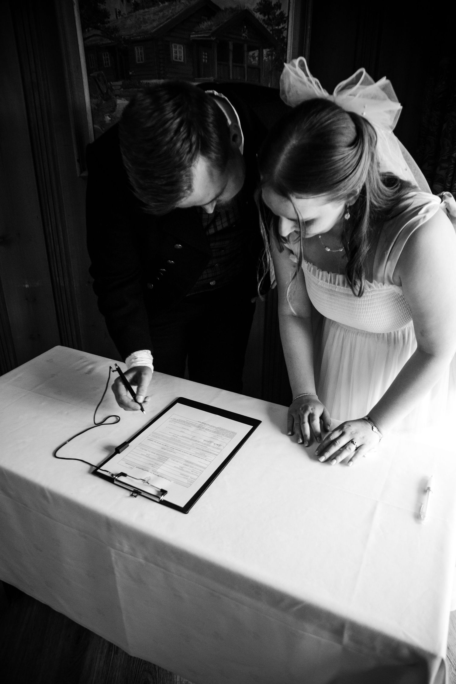Person in white signing documents at a table in dramatic black and white lighting.