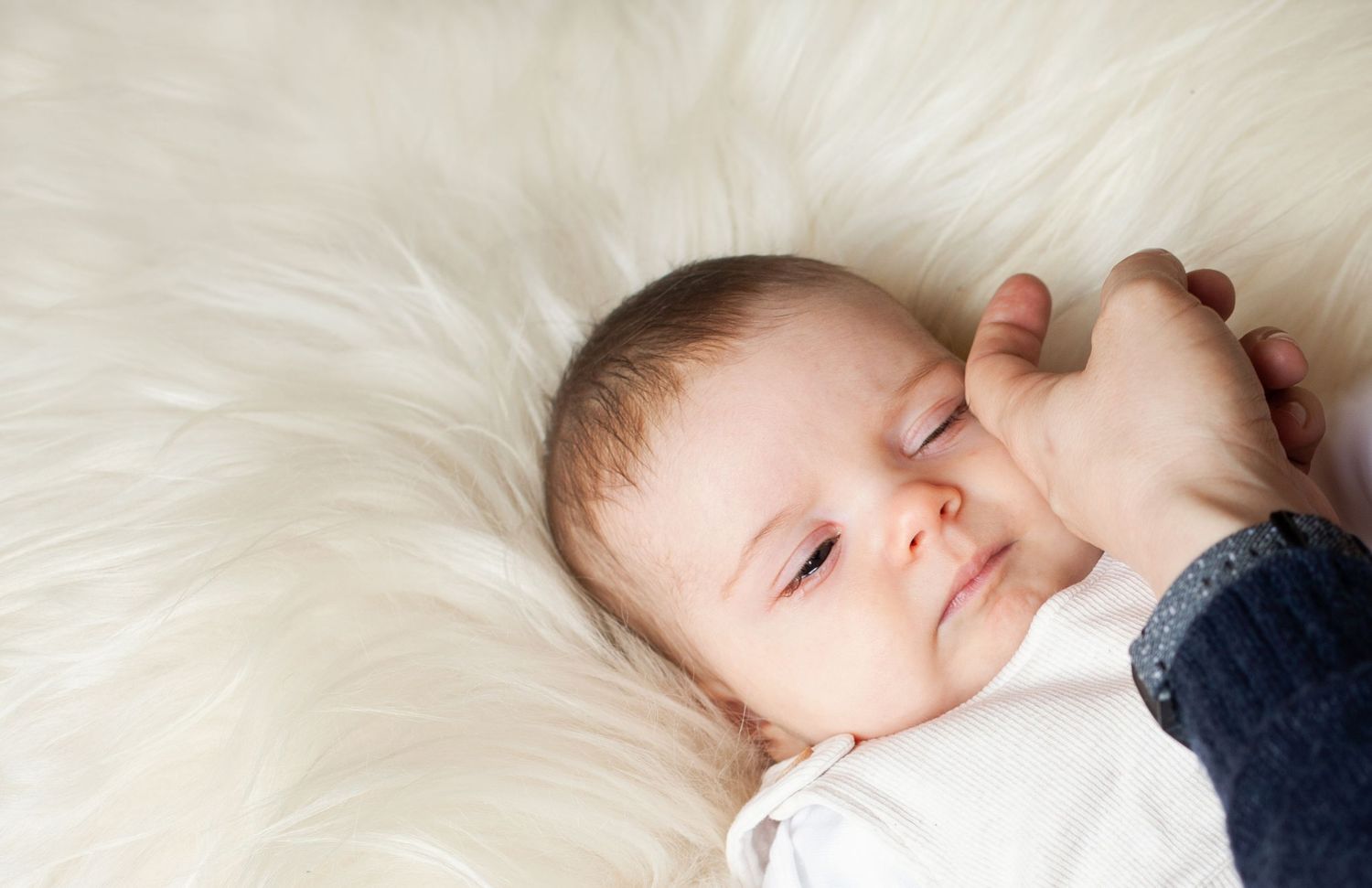 A sleeping baby rests peacefully on soft white fur bedding.