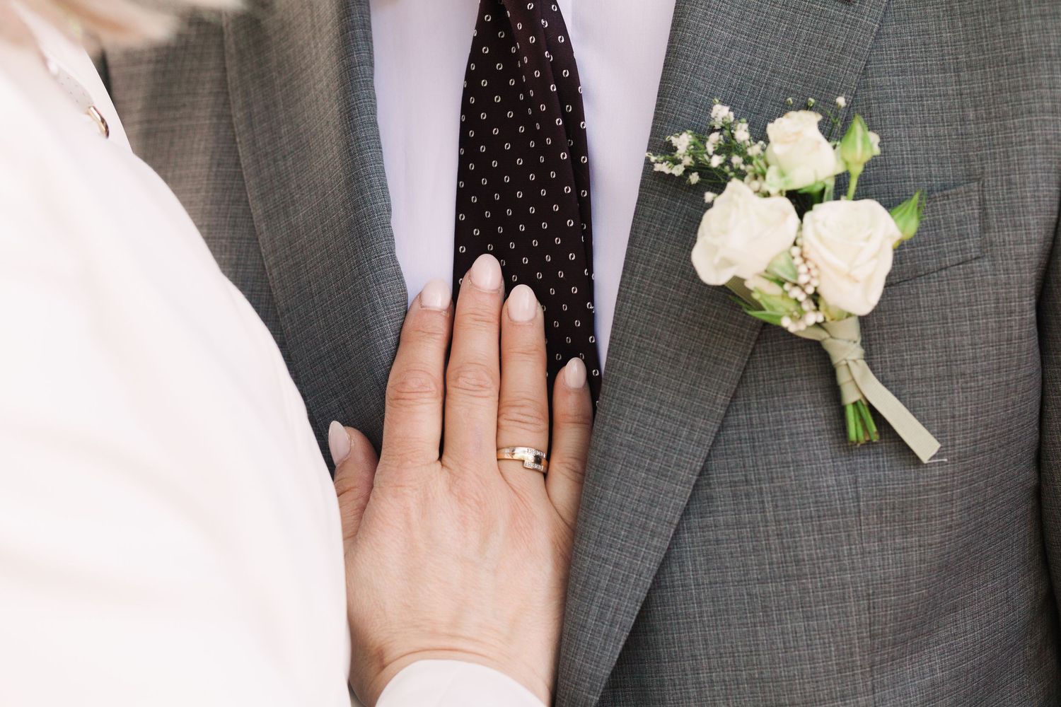 Close-up of hands wearing wedding rings against a gray suit background.