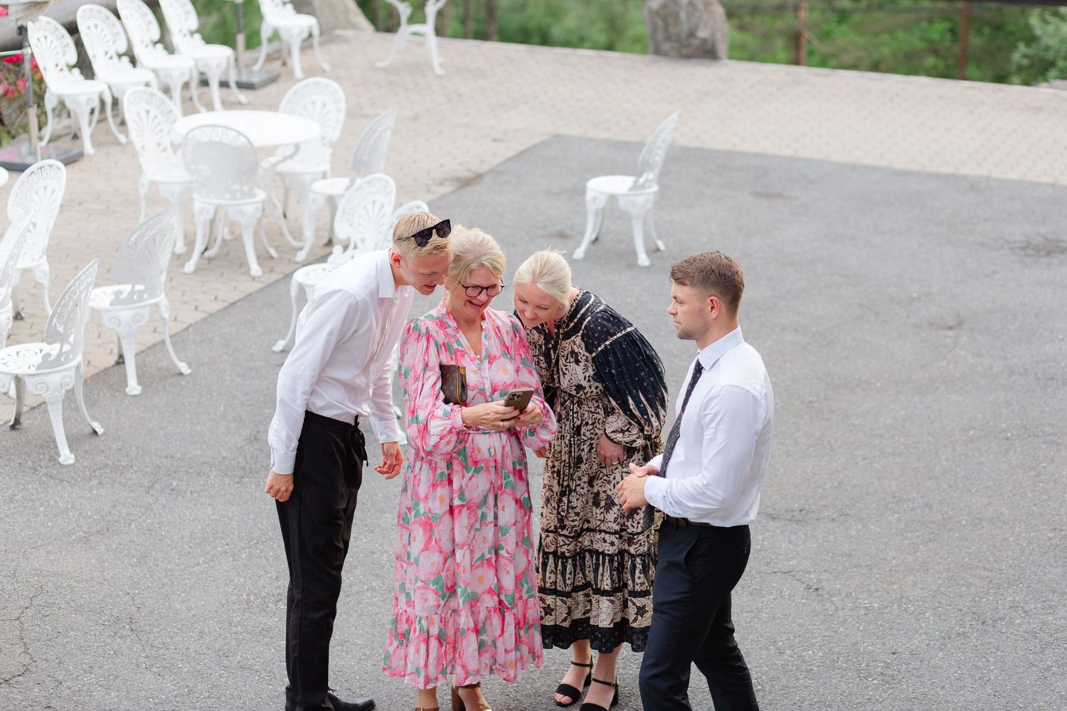 A small group gathered outdoors on a patio with white chairs having an animated discussion.