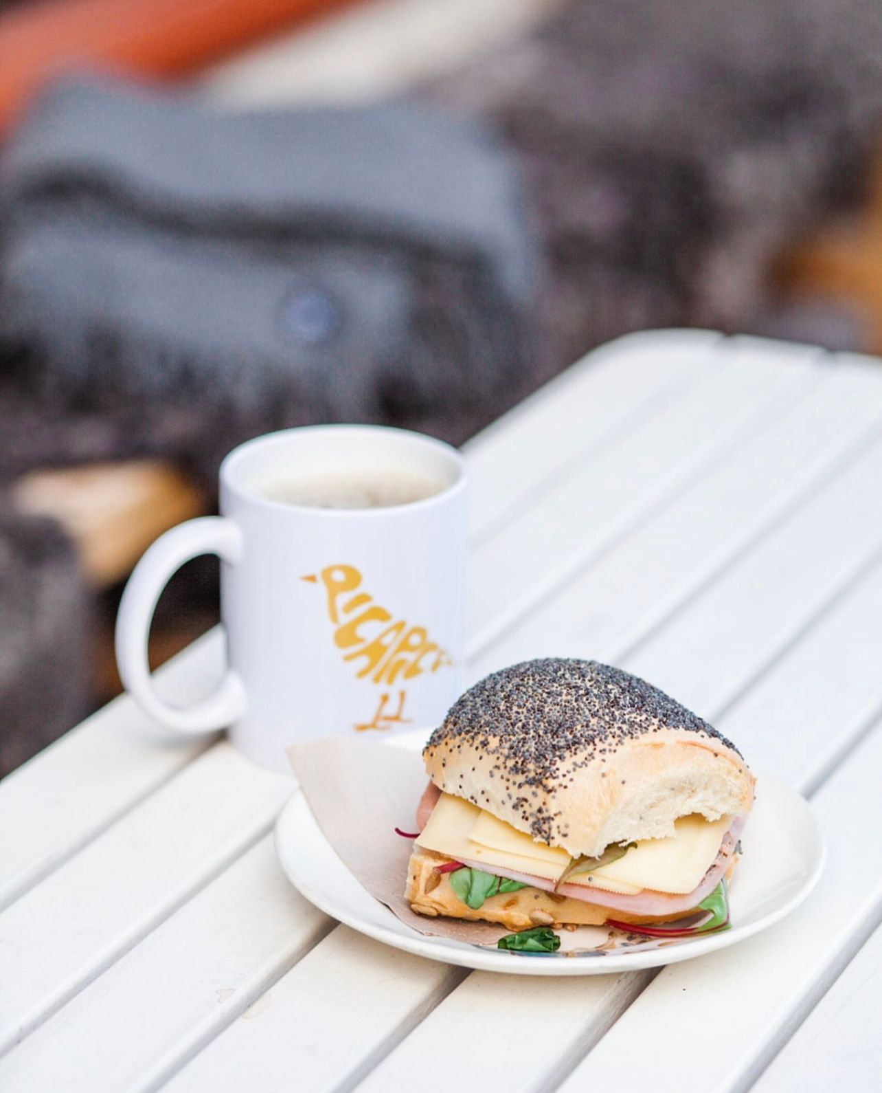 White ceramic coffee cups and sandwiches arranged on a wooden outdoor table surface.