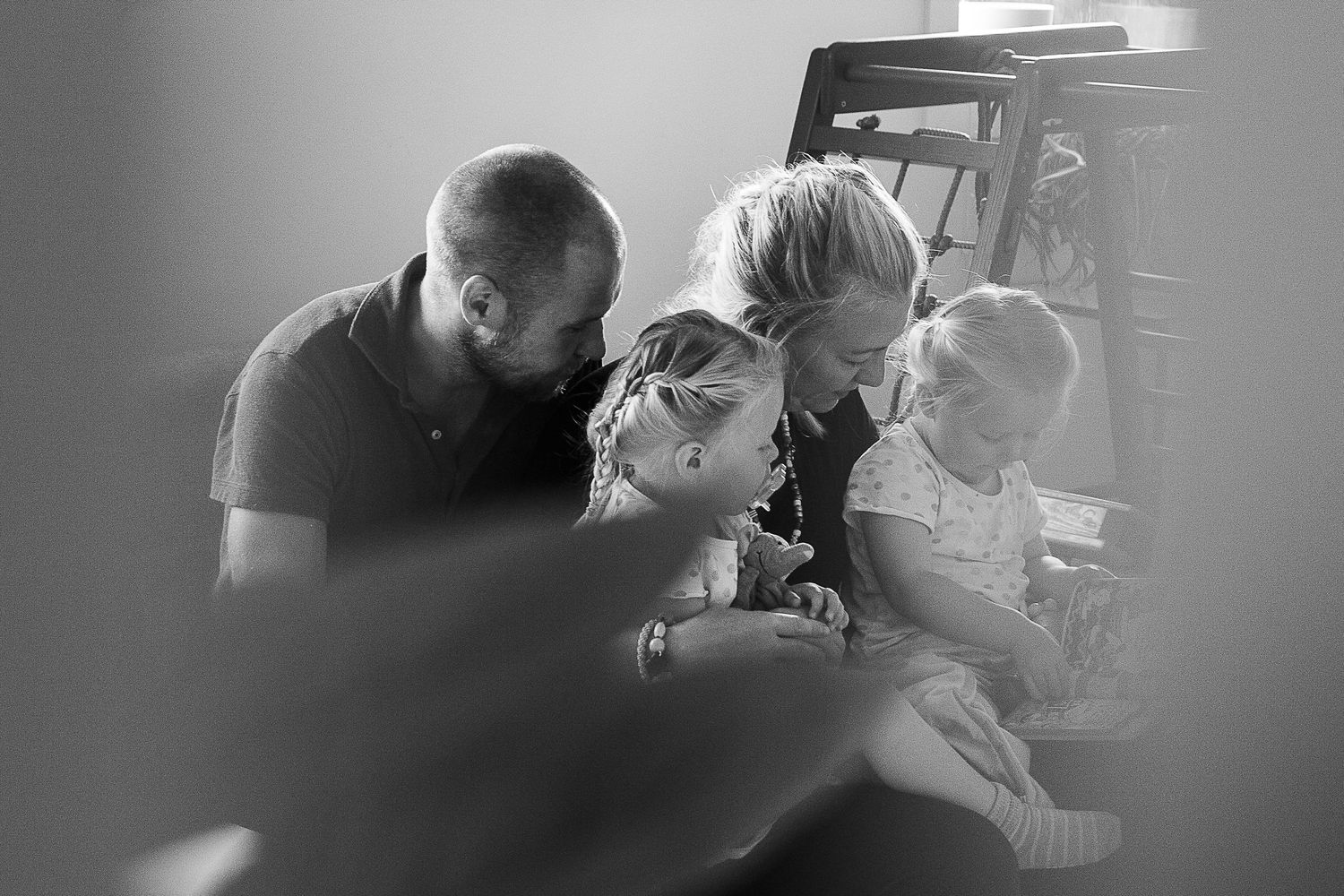 An intimate black and white family moment captured through a blurred foreground.