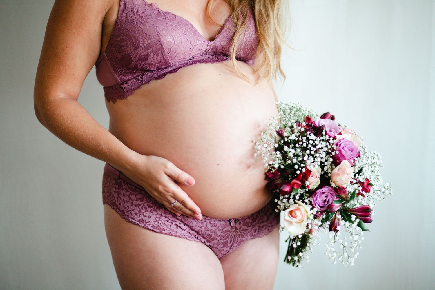 Maternity boudoir photos with purple lace lingerie and floral bouquet accents.