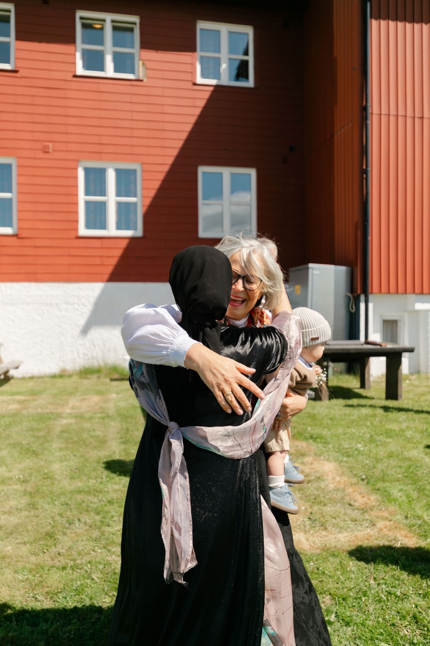 People embrace in front of a red building on a sunny day.