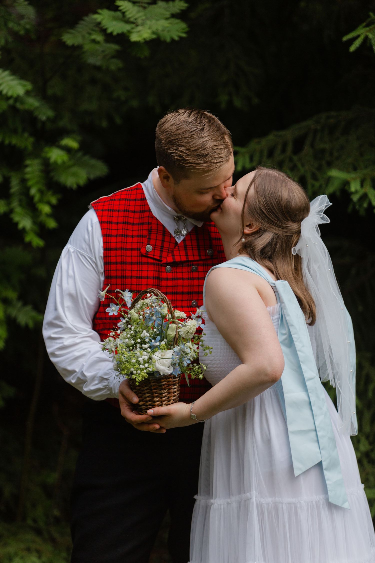 A couple in wedding attire sharing a romantic moment while holding a basket of wildflowers.
