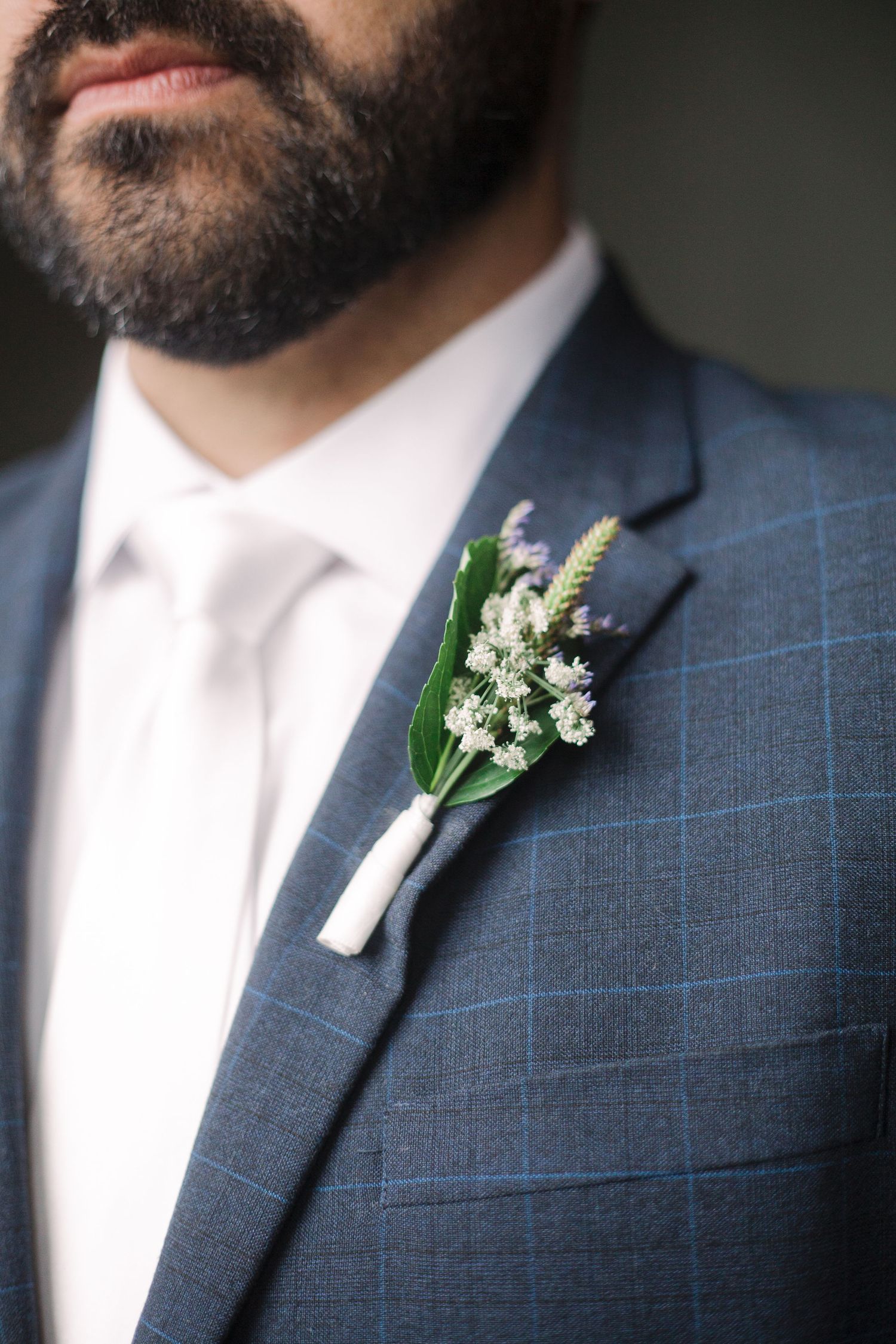 Close-up details of a navy checkered suit with lily of the valley boutonniere.