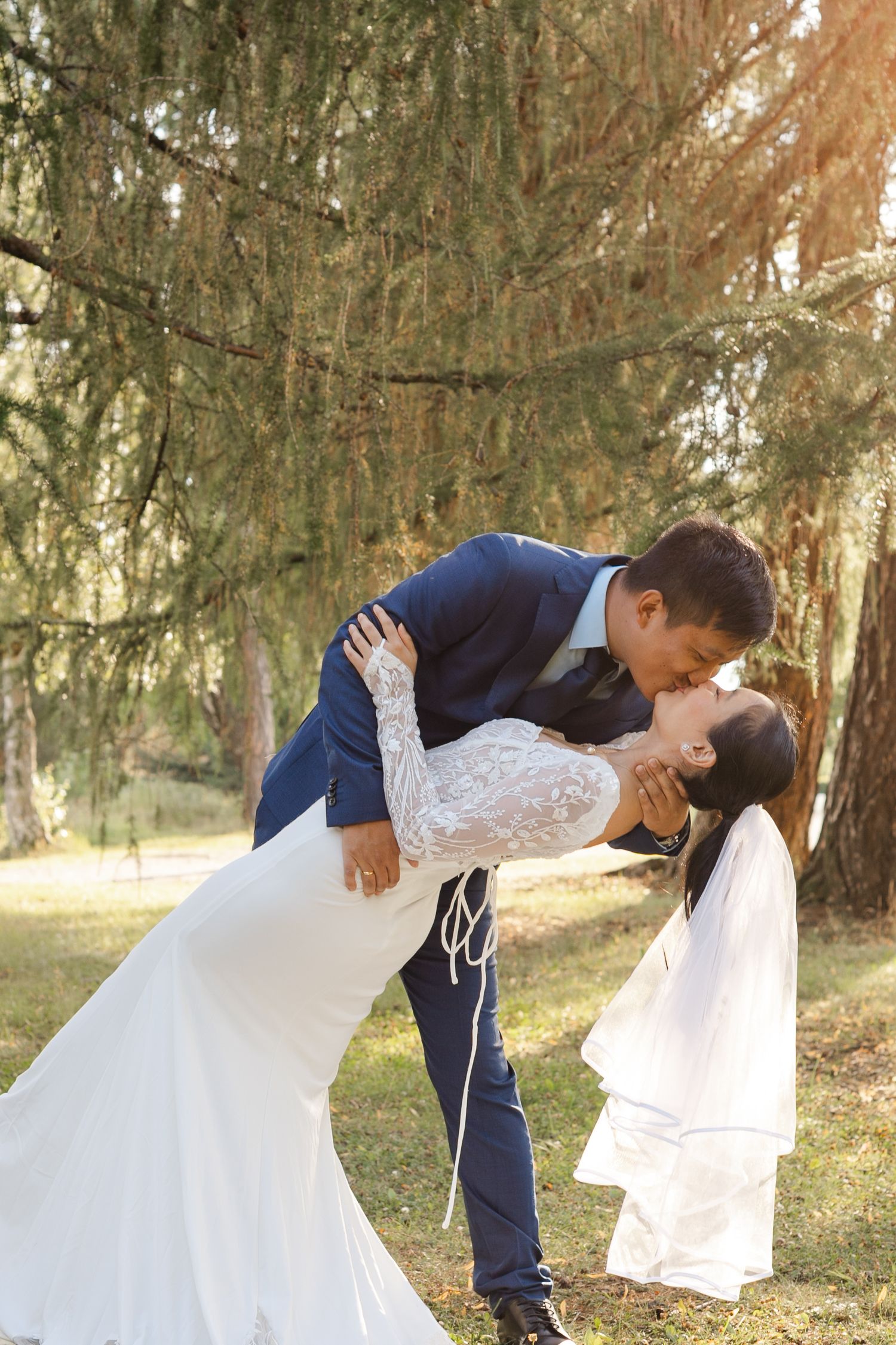 A romantic dip pose between newlyweds in a wooded setting.