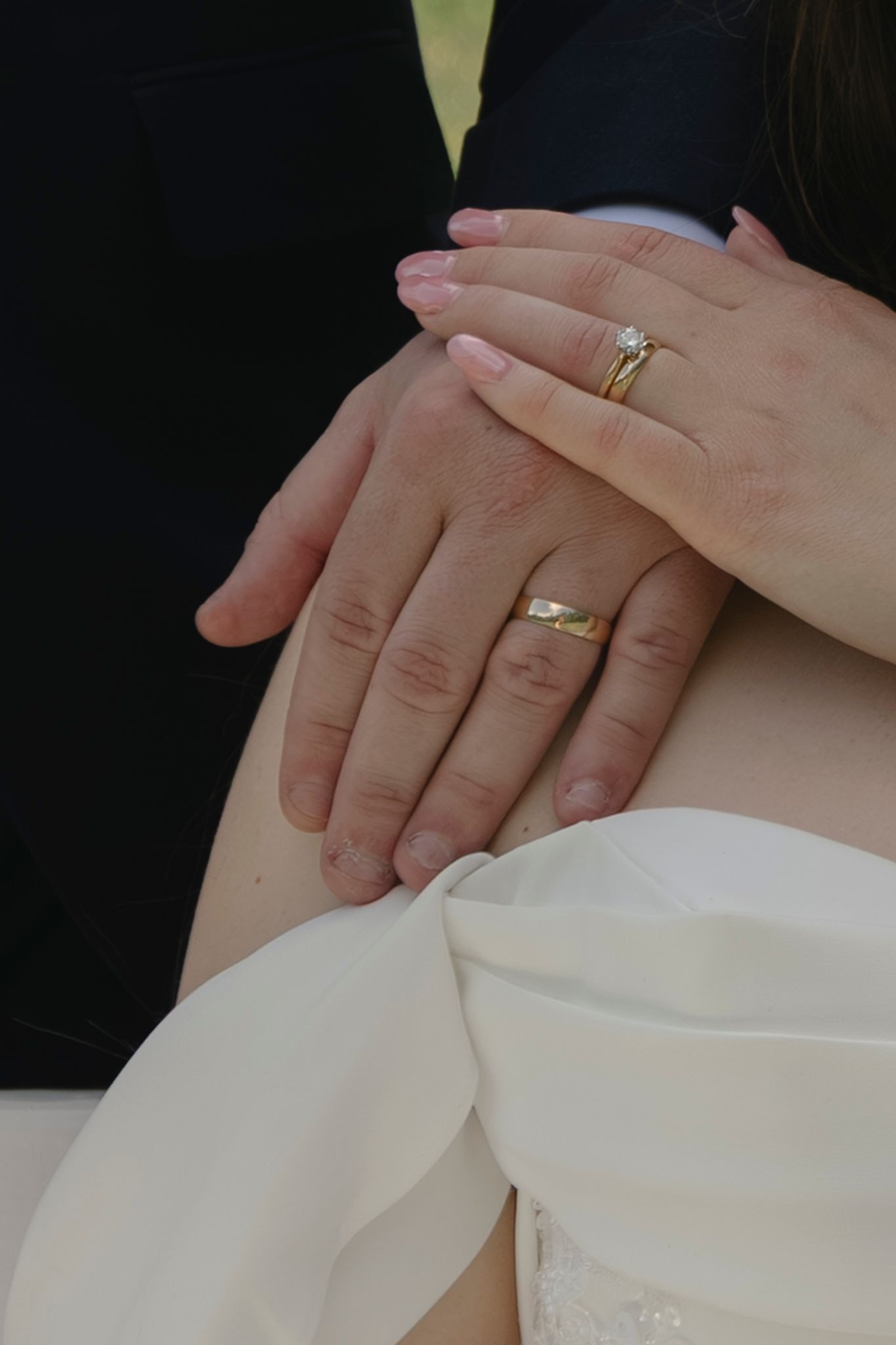 Newlywed couple displaying wedding rings, bride wearing diamond engagement ring and groom with gold band, hands resting together.