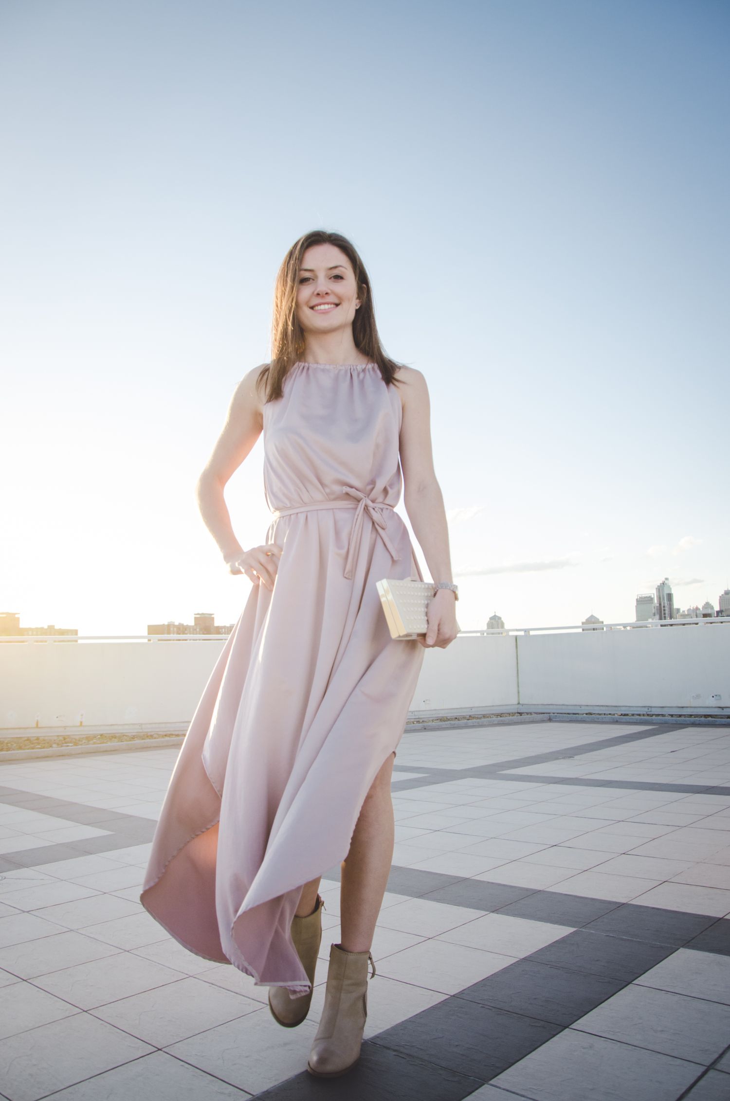 A flowing pink dress twirls gracefully against a bright sky and tiled rooftop setting during a sunset photoshoot.