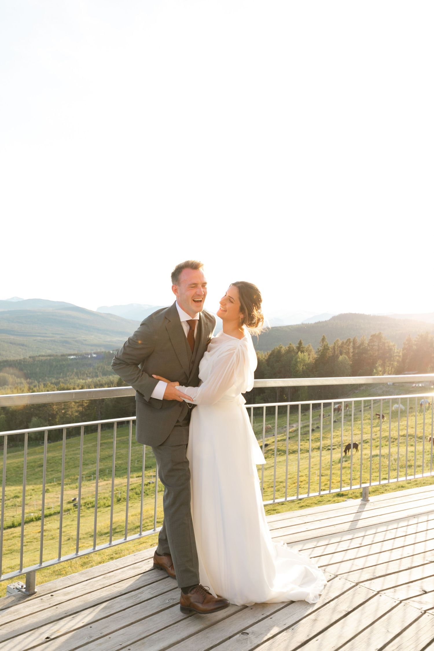 Joyful wedding couple laughing together on outdoor deck with mountain vista.