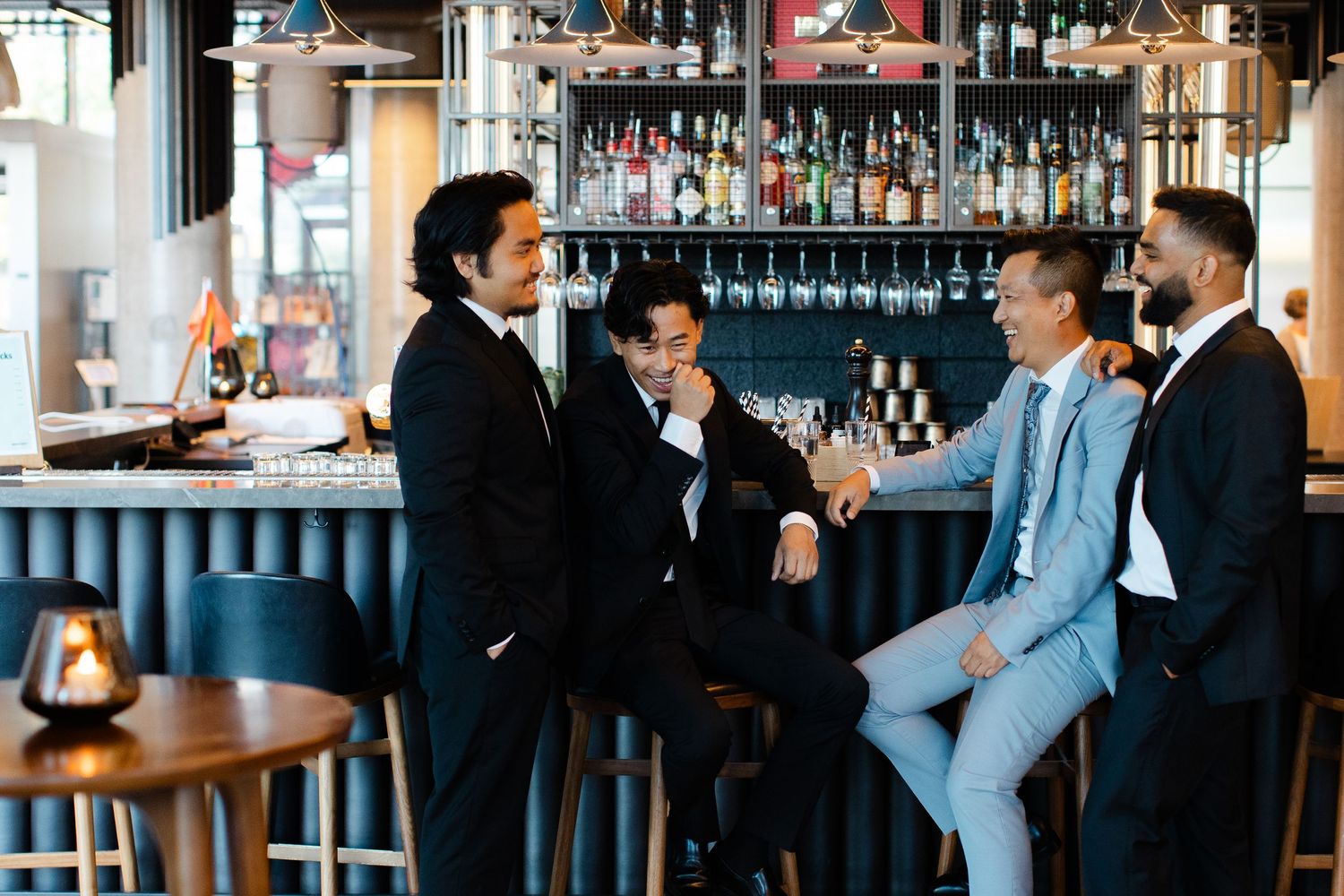 Wedding party members in suits gathered at an elegant bar with bottles and glasses.
