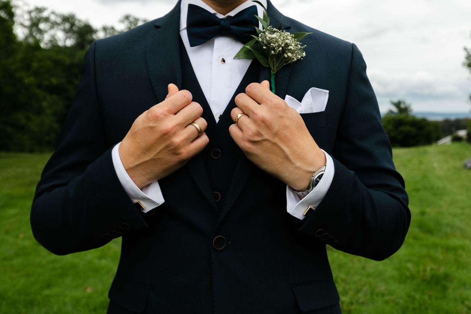 Groom adjusts bowtie while wearing classic black tuxedo outdoors.