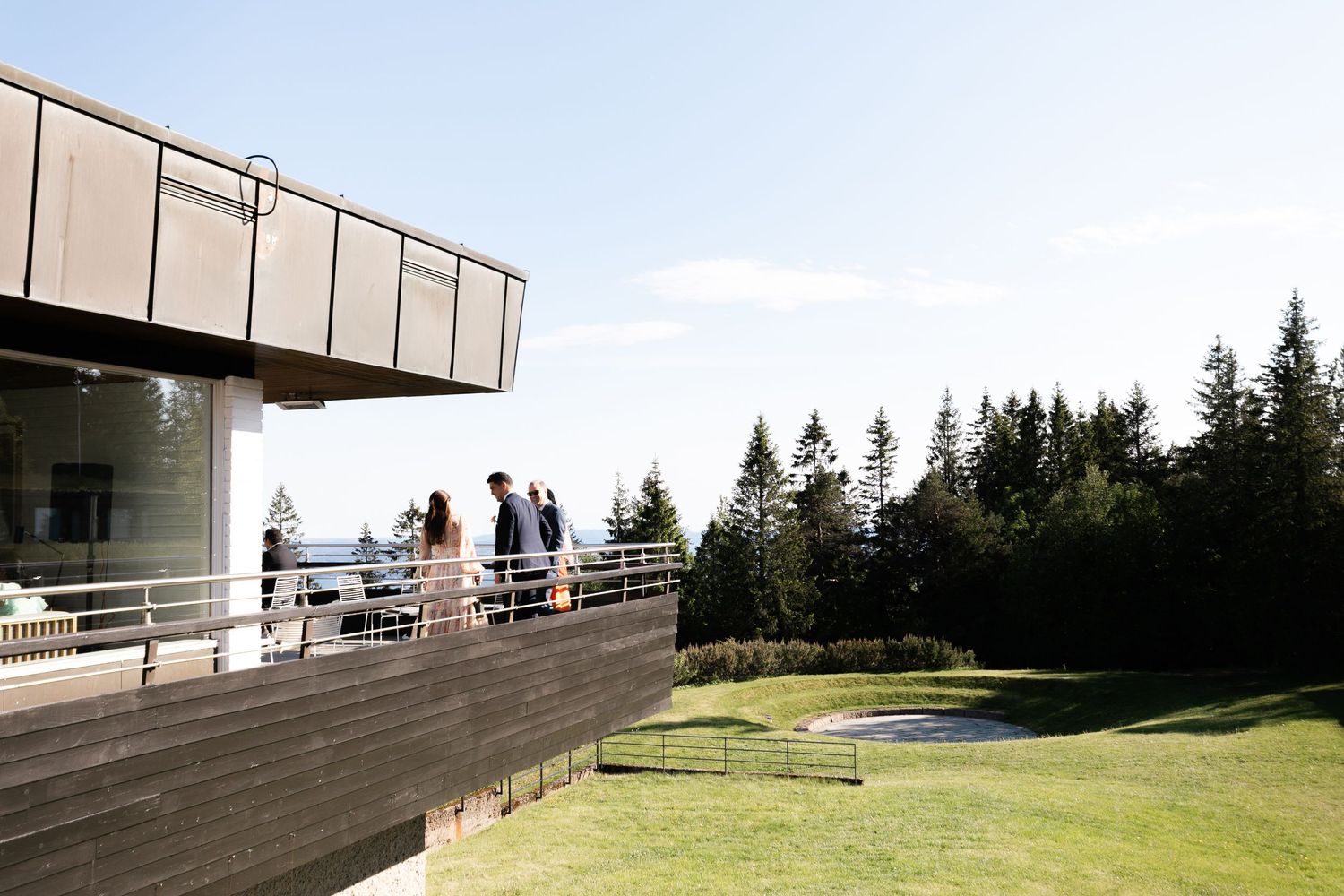 A panoramic view of a modern building with wooden decking and scenic mountain vistas in the background.