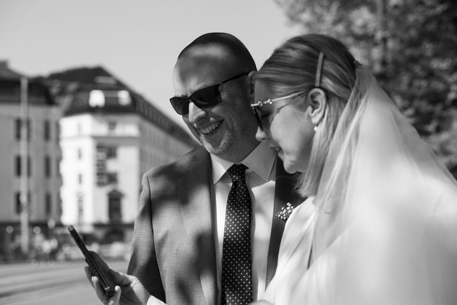 Wedding party members gather outdoors in formal attire on a sunny day.