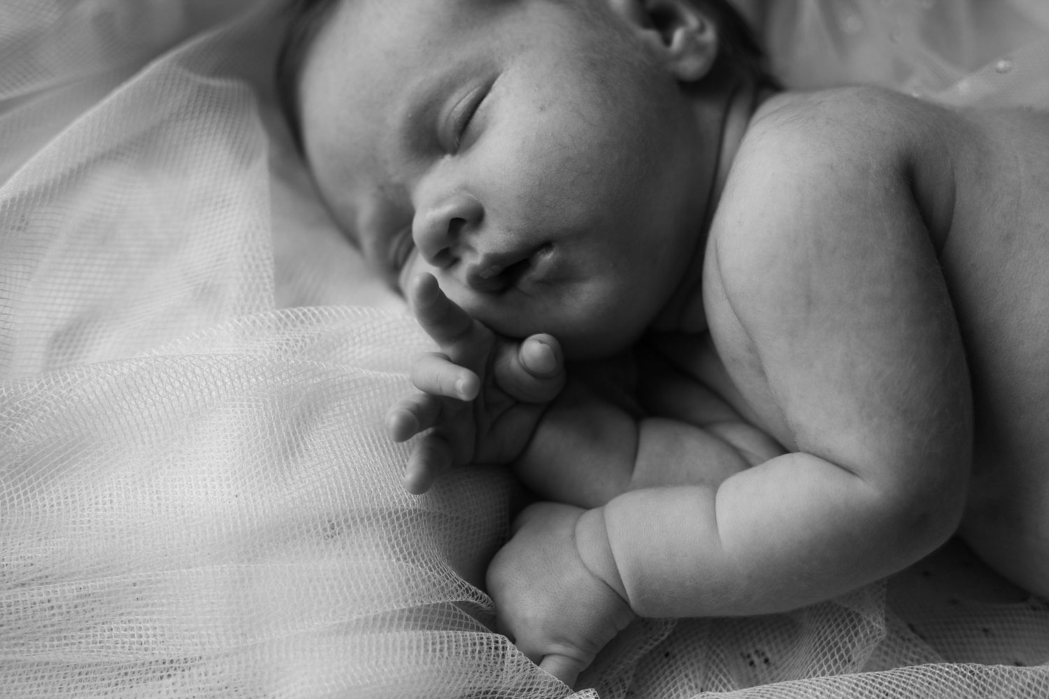 Peaceful black and white image of sleeping newborn on white bedding.