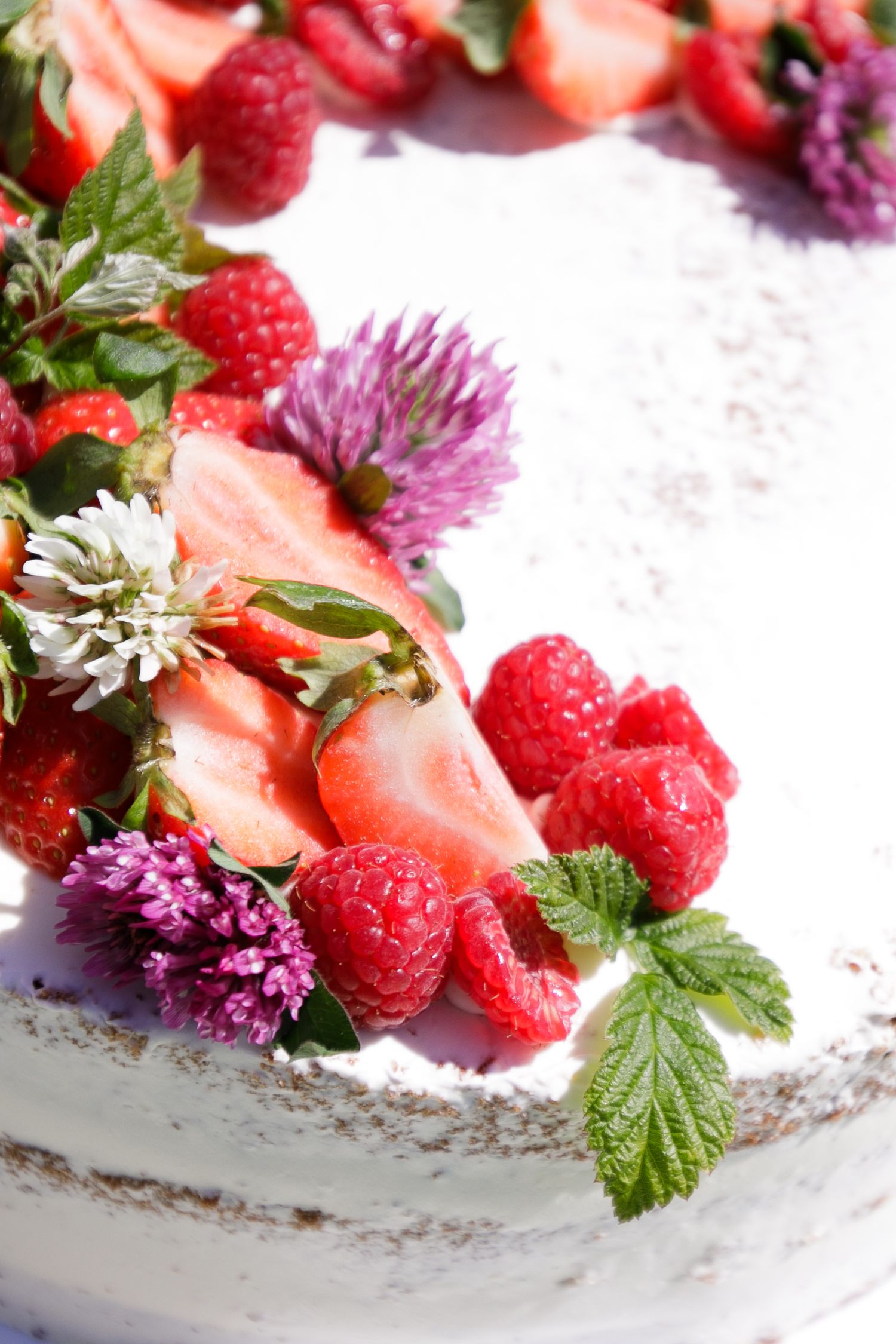 Fresh strawberries and raspberries garnished with purple flowers on a white dessert.