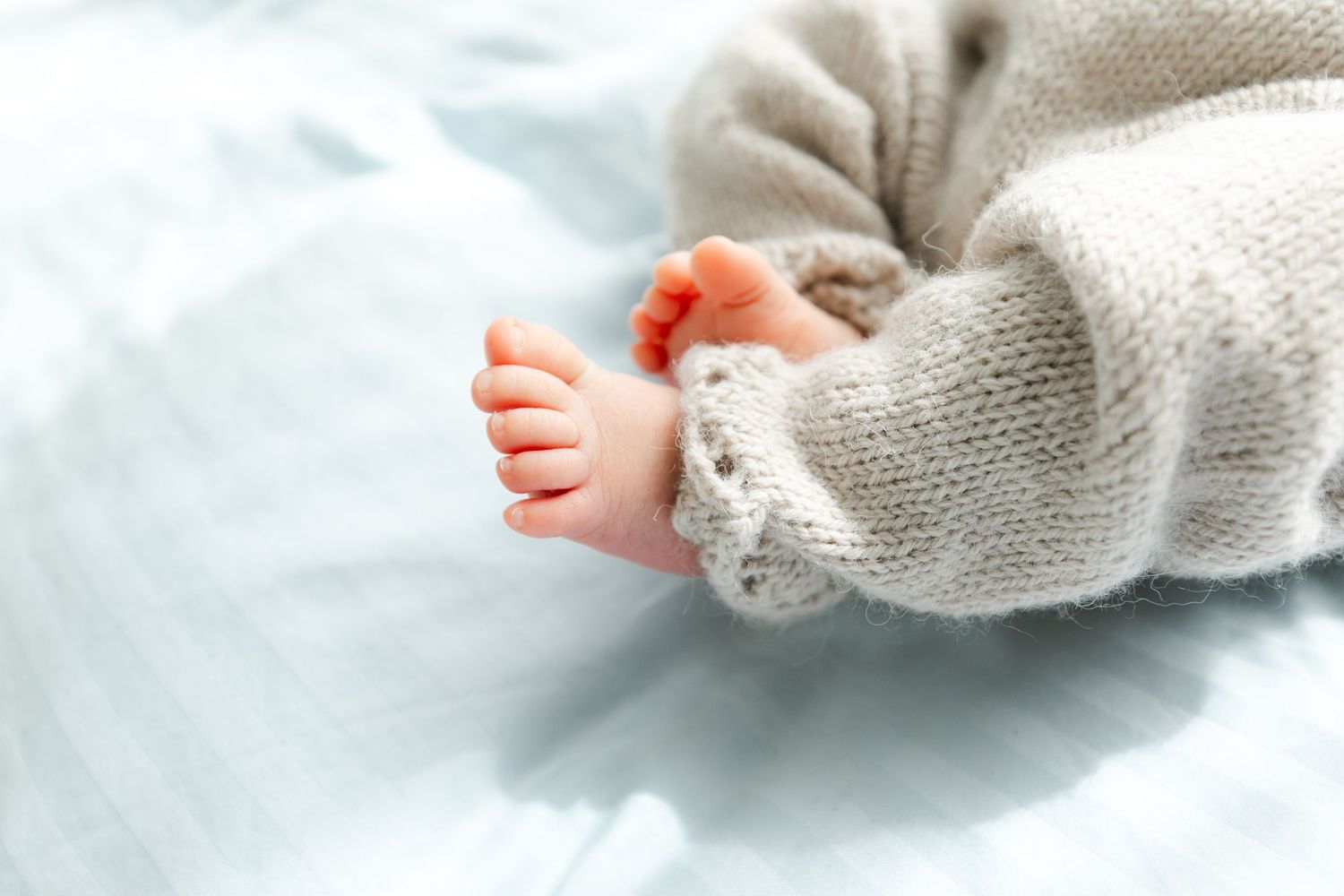 Detail shots of tiny feet in a soft knit sweater against white bedding.