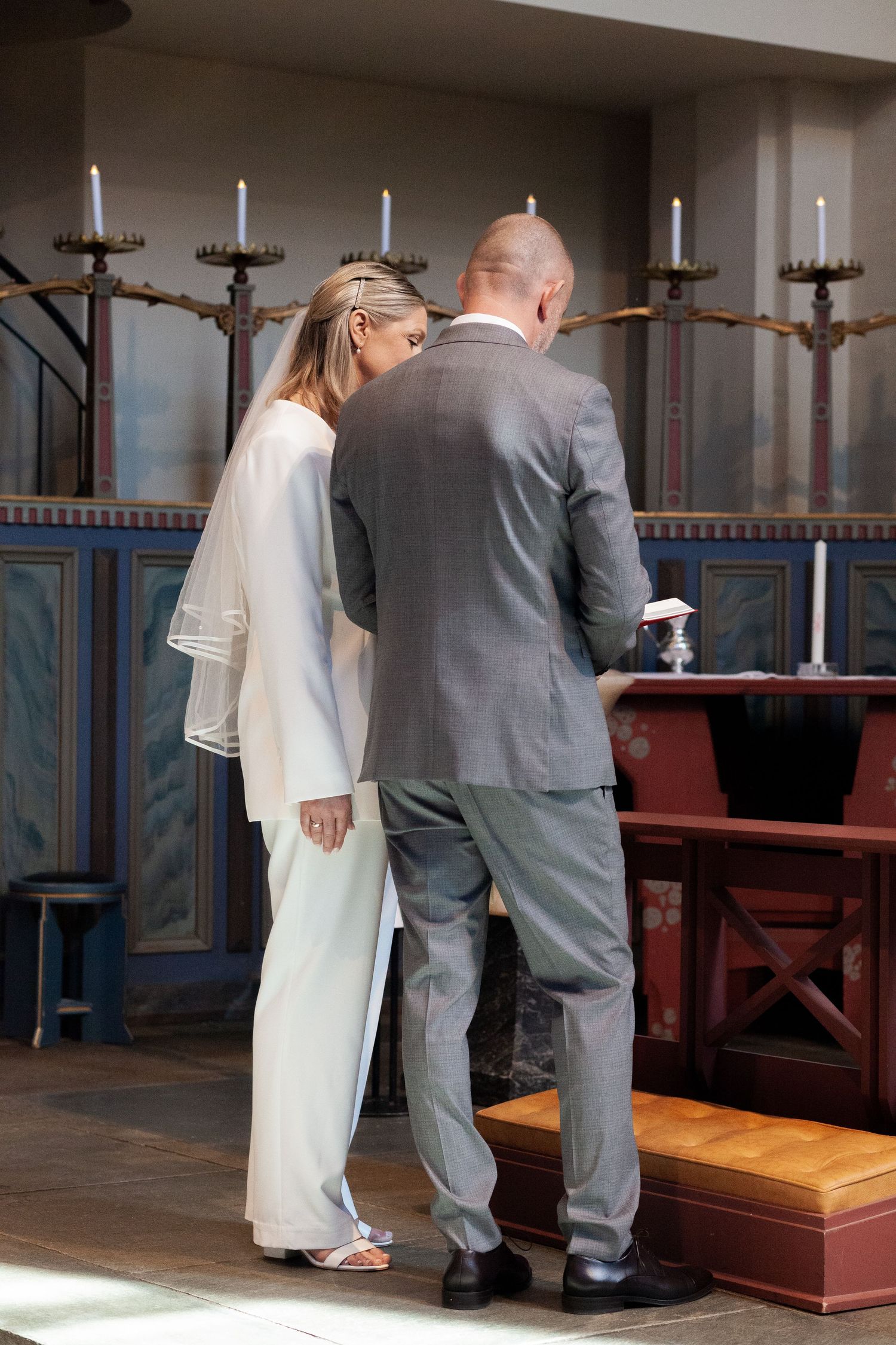 A couple standing in a church interior with blue decorative walls and wooden pews.