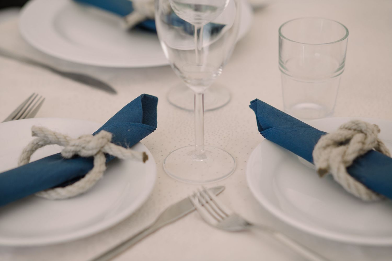 Clean table settings with white plates, blue napkins and wine glasses.