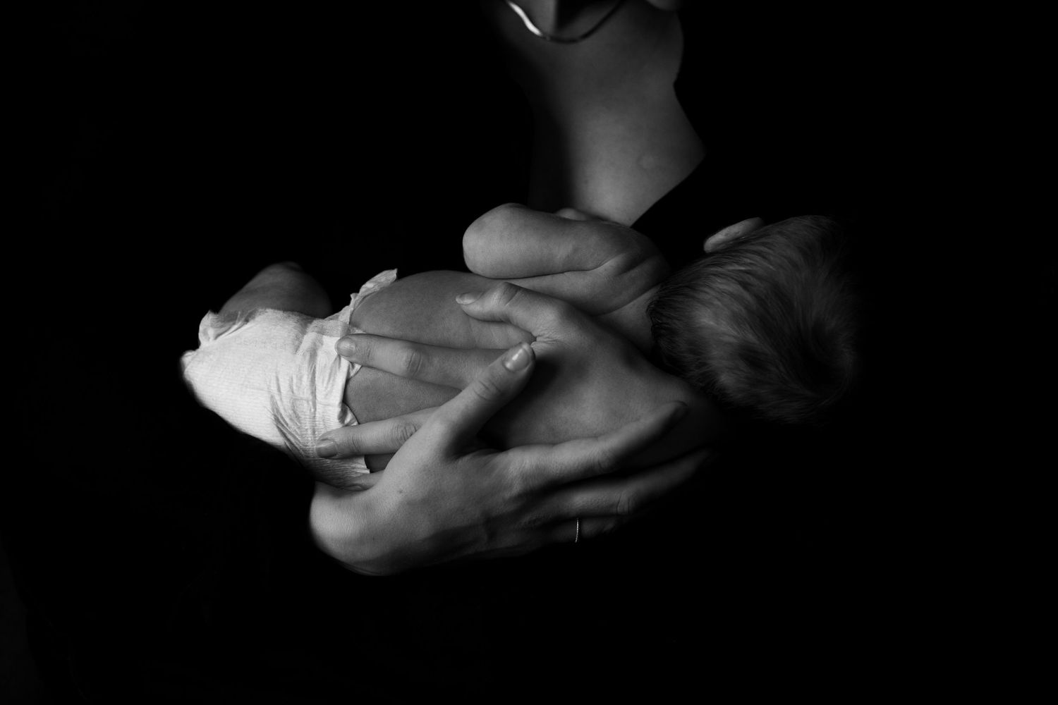 Black and white image of hands tenderly holding a sleeping newborn.