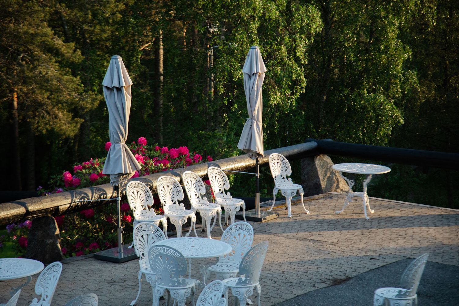 Elegant outdoor wedding reception setup with white chairs and umbrellas on a stone patio surrounded by greenery.
