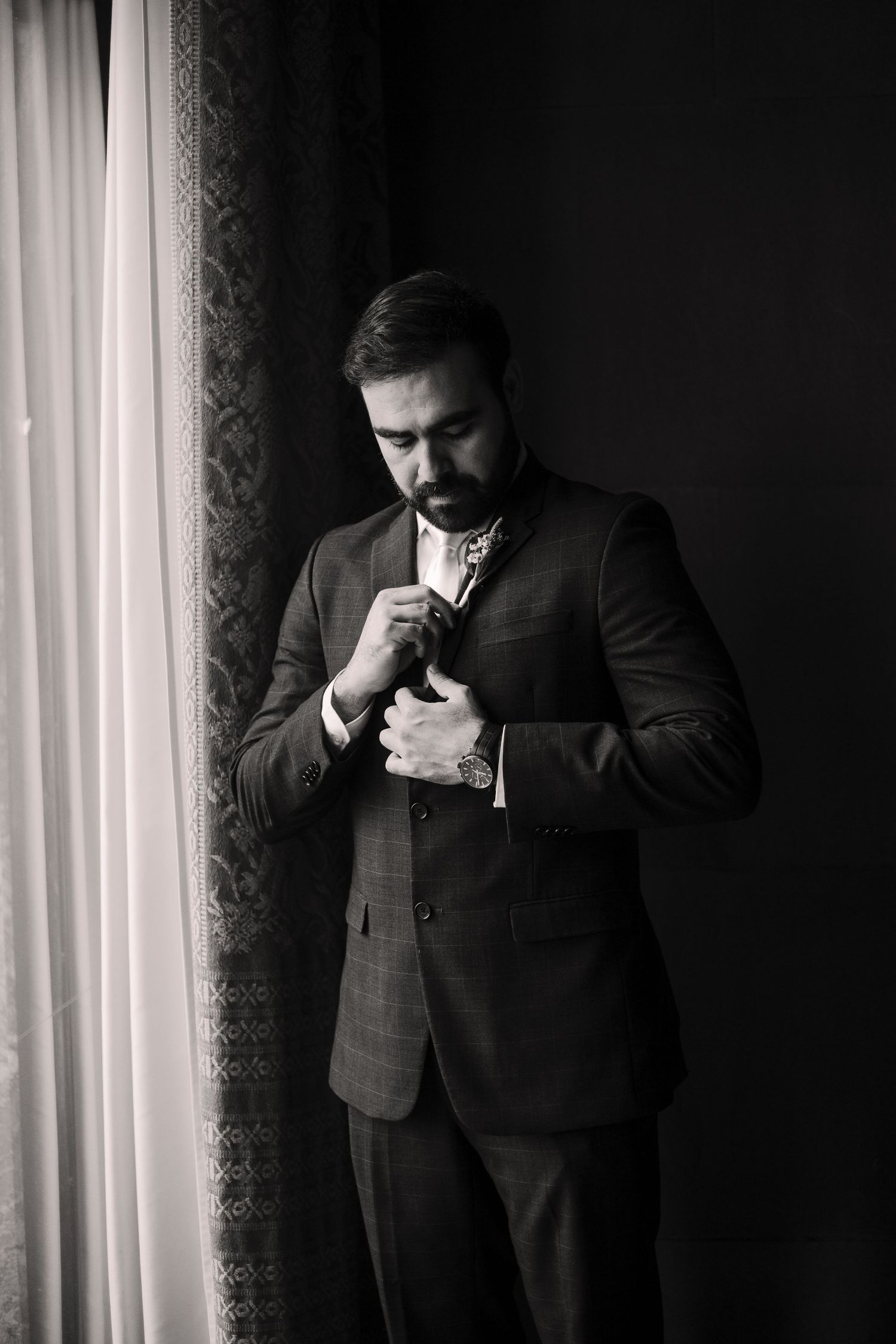 Dramatic black and white photos of a groom adjusting his tie.
