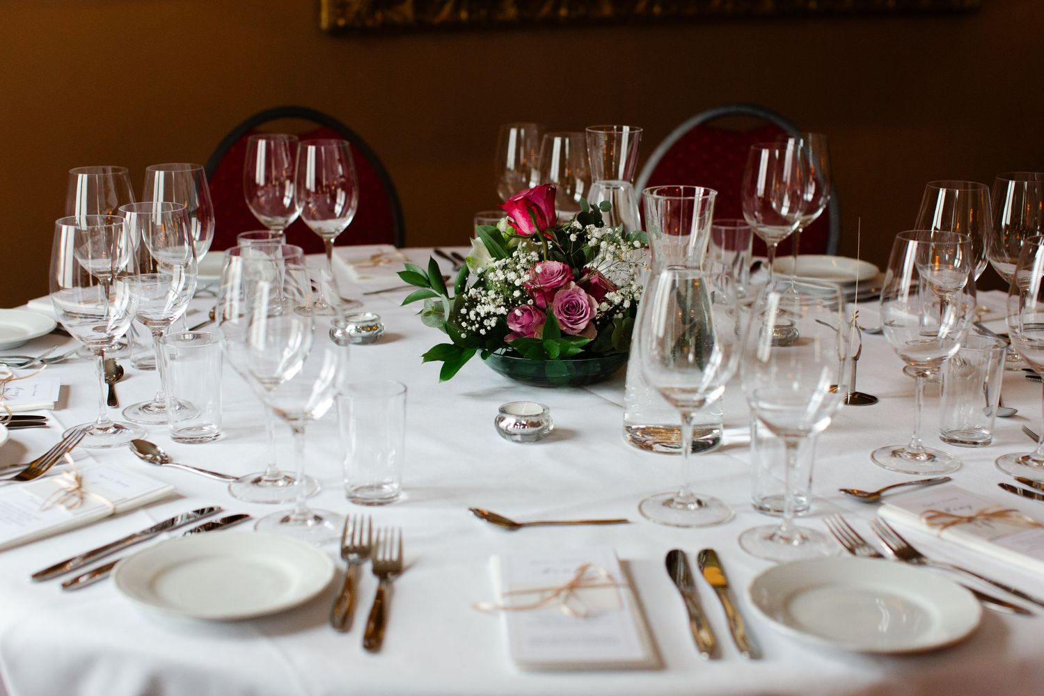 Elegant wedding reception table setting with crystal wine glasses, white linens, silverware, and a pink floral centerpiece.