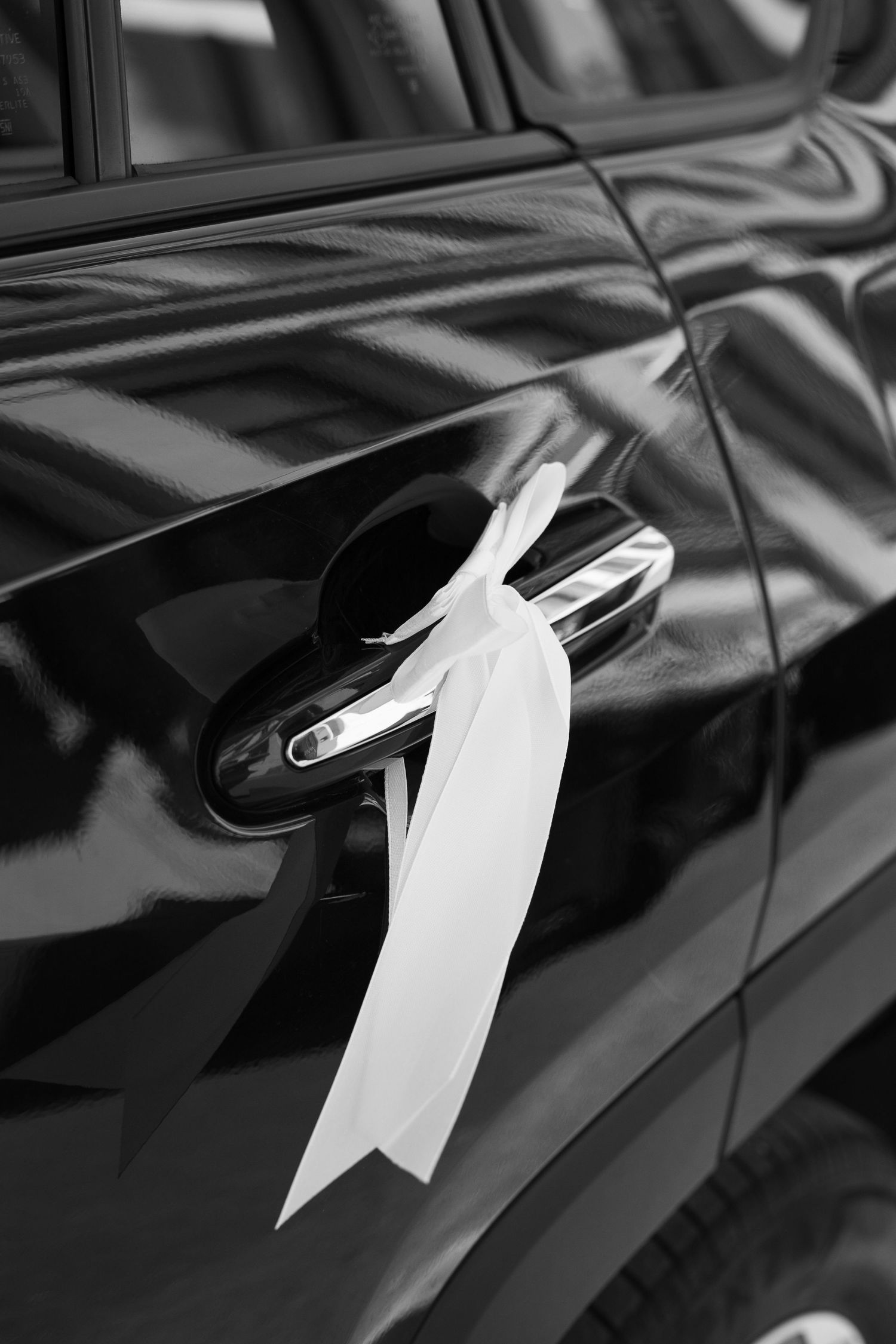 A white ribbon decorates the door handle of a sleek black car.