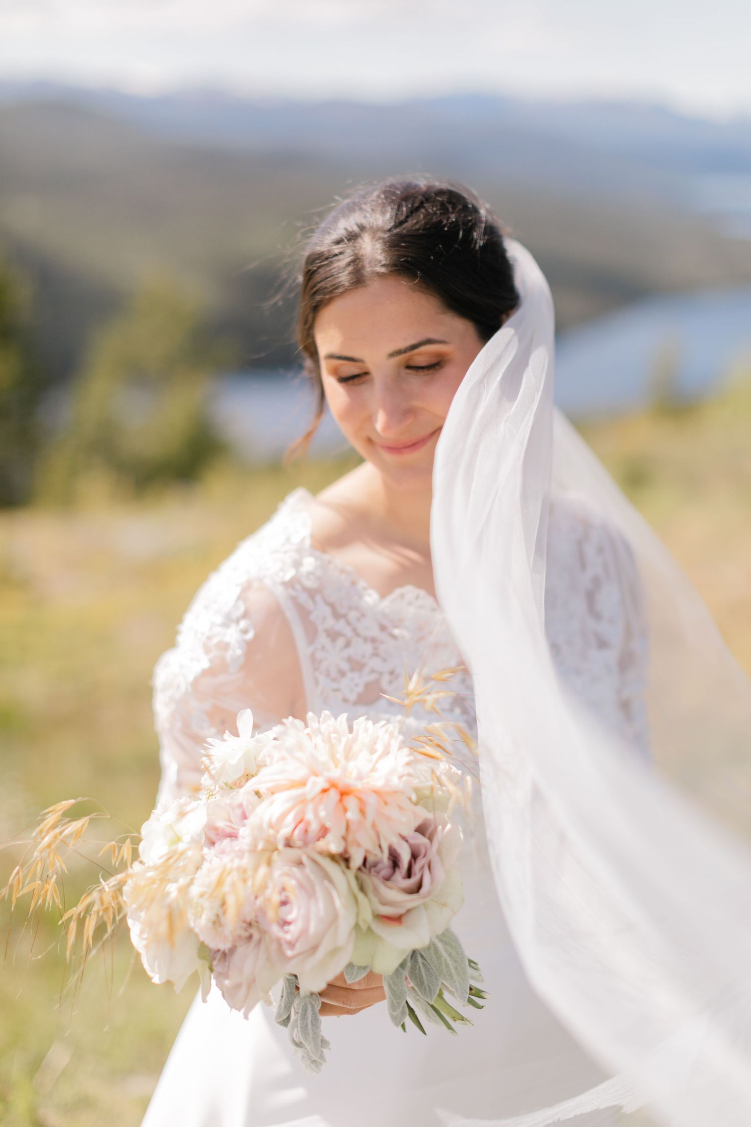 Delicate pink and blush wedding bouquet with flowing white veil against mountain backdrop.