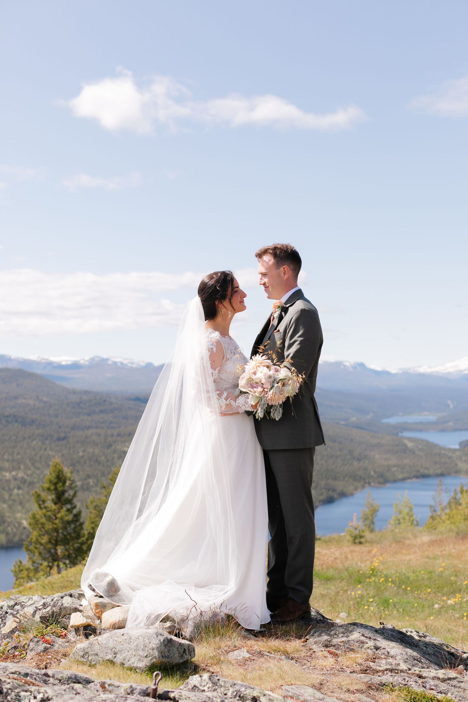 Wedding portraits on mountainside with lake and dramatic mountain ranges in background.