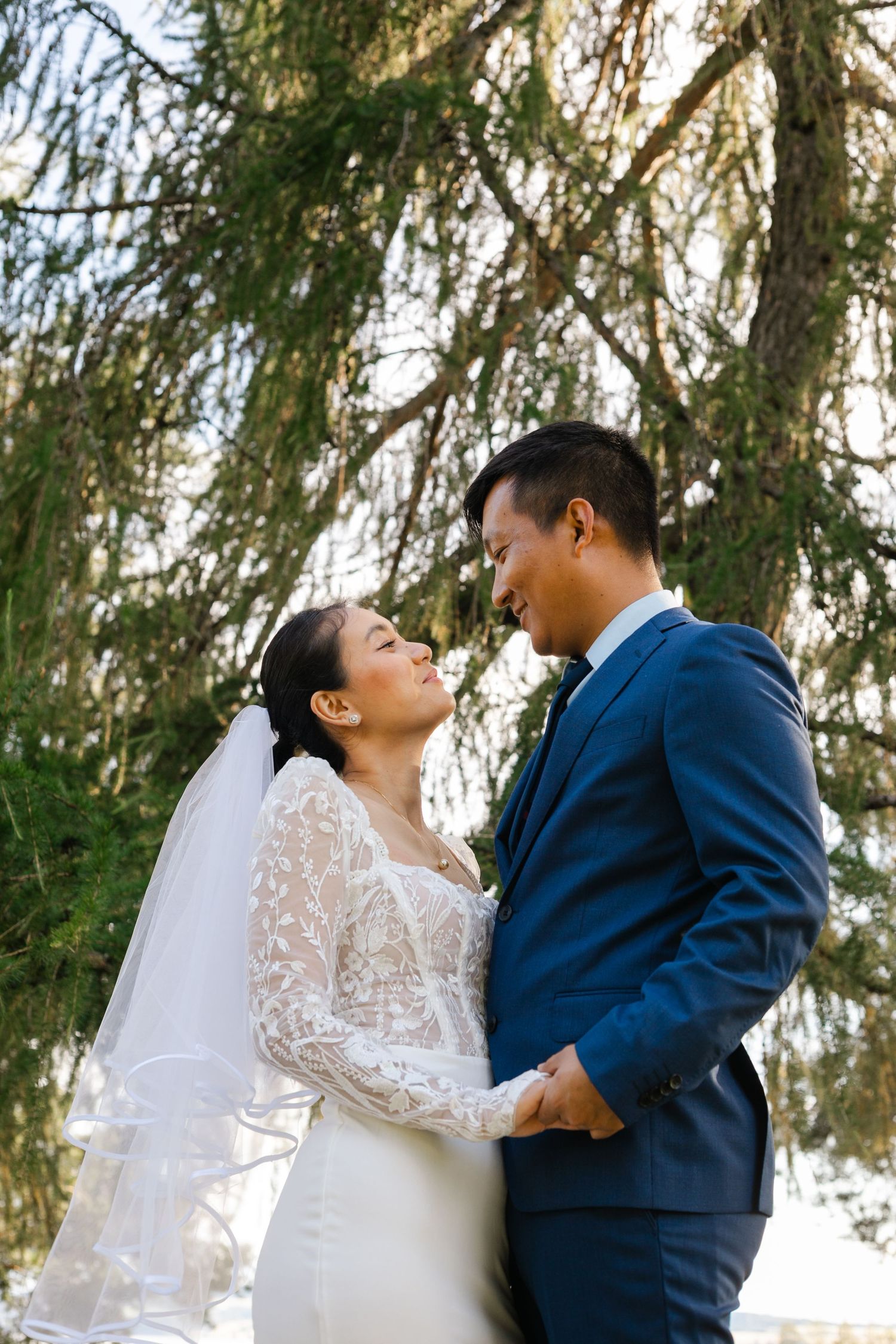 A couple in wedding attire sharing an intimate moment under a weeping willow tree.