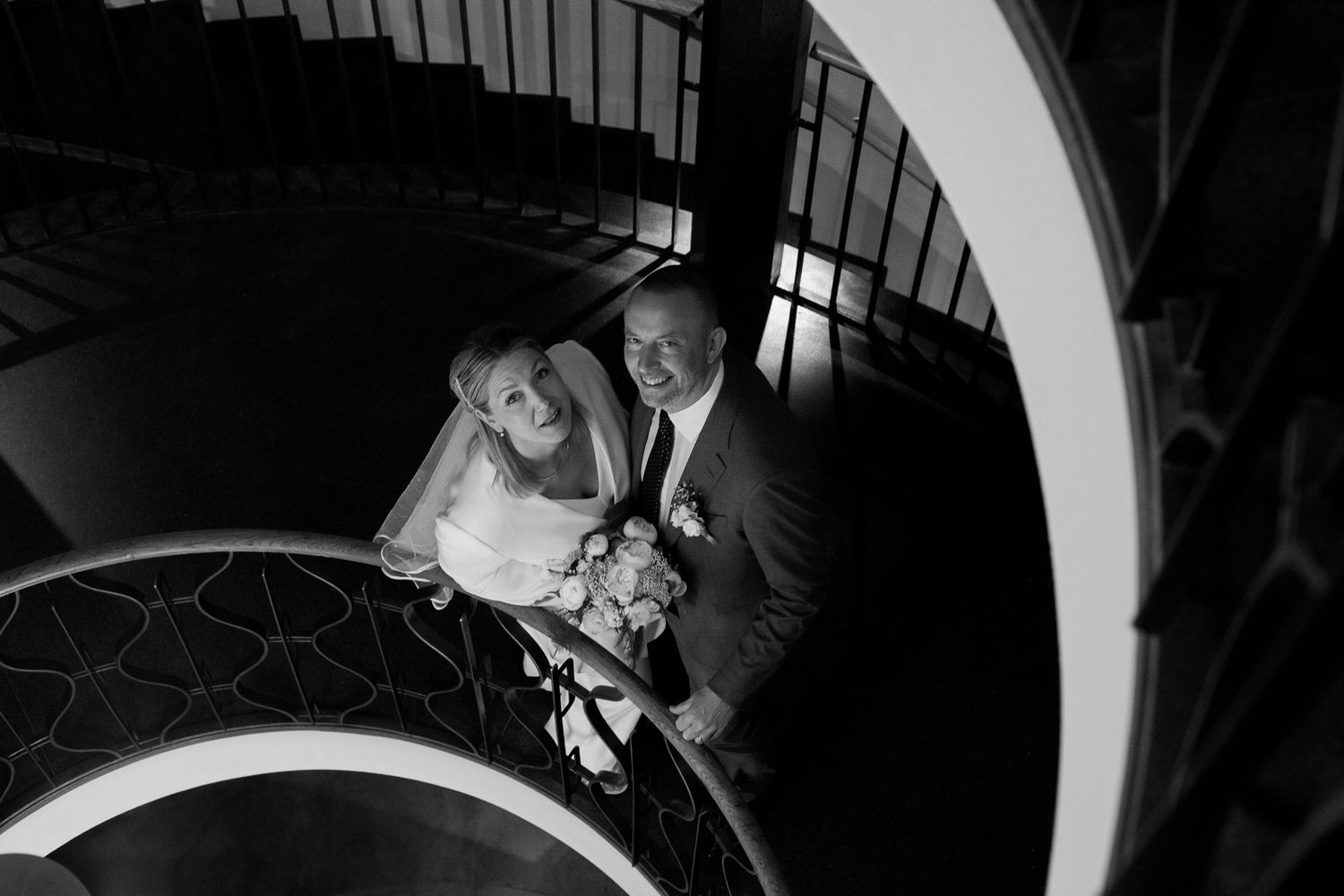 A black and white photograph of a couple on a staircase during what appears to be a wedding celebration.