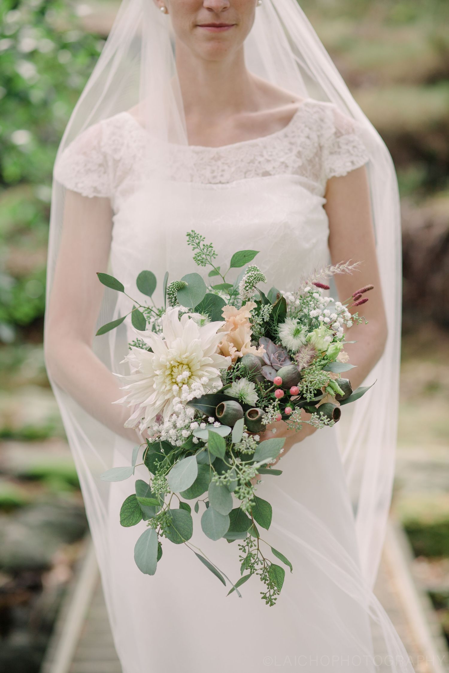 Wedding bouquet with white flowers, eucalyptus, and greenery against white dress.