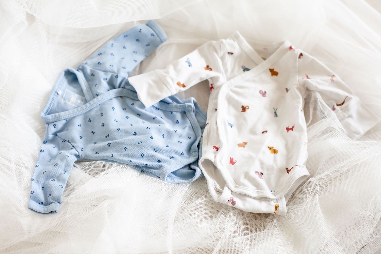 Collection of soft baby clothes in white and blue tones laid on white background.