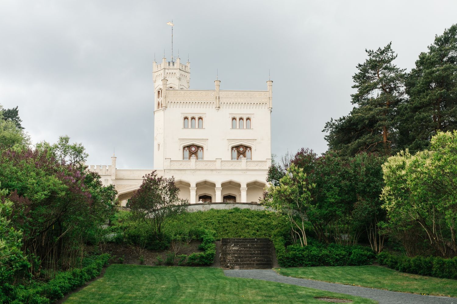 White castle-like wedding venue surrounded by green trees under a cloudy sky.