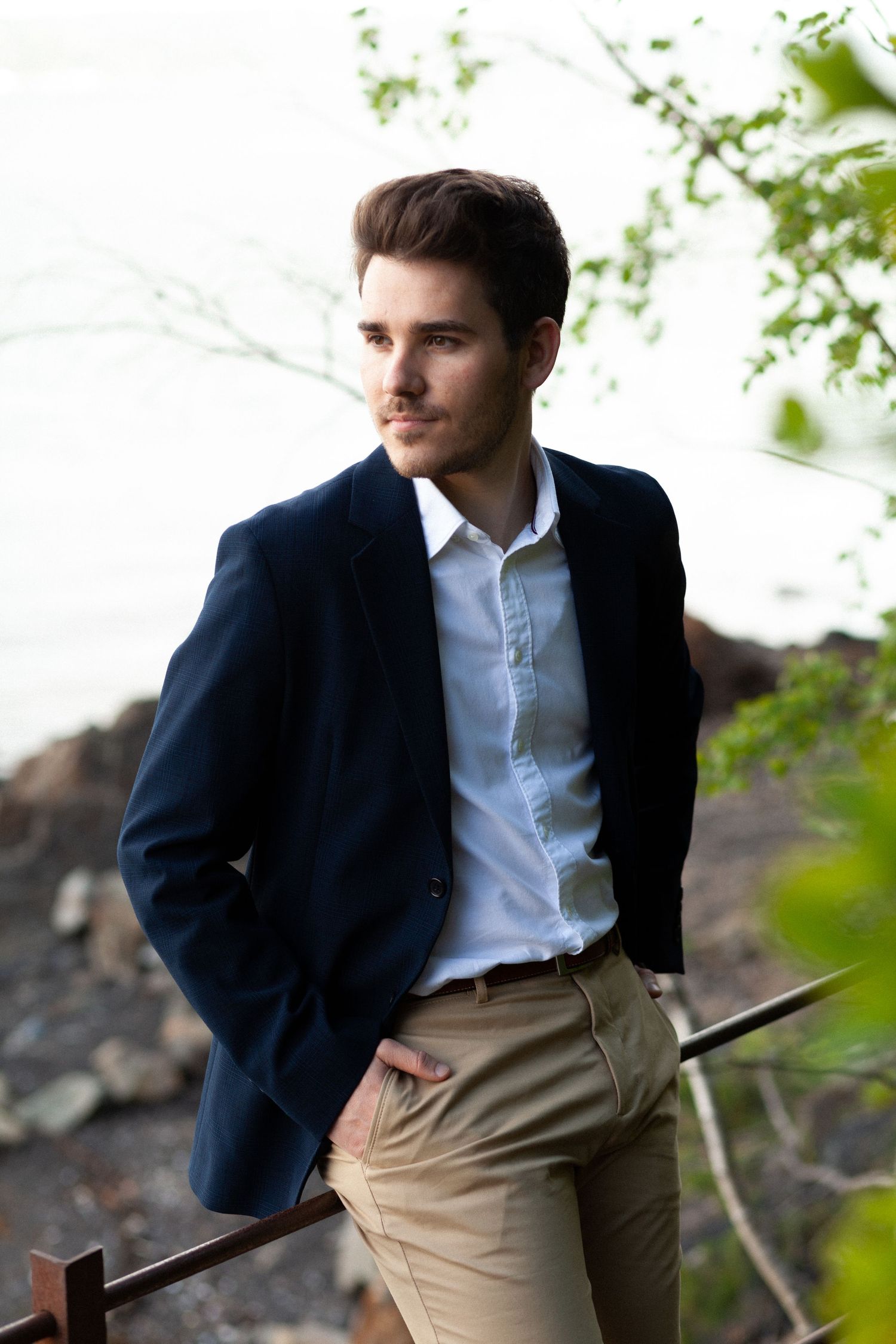 Professional wearing a navy blazer and khaki pants poses against a natural outdoor backdrop with blurred foliage.